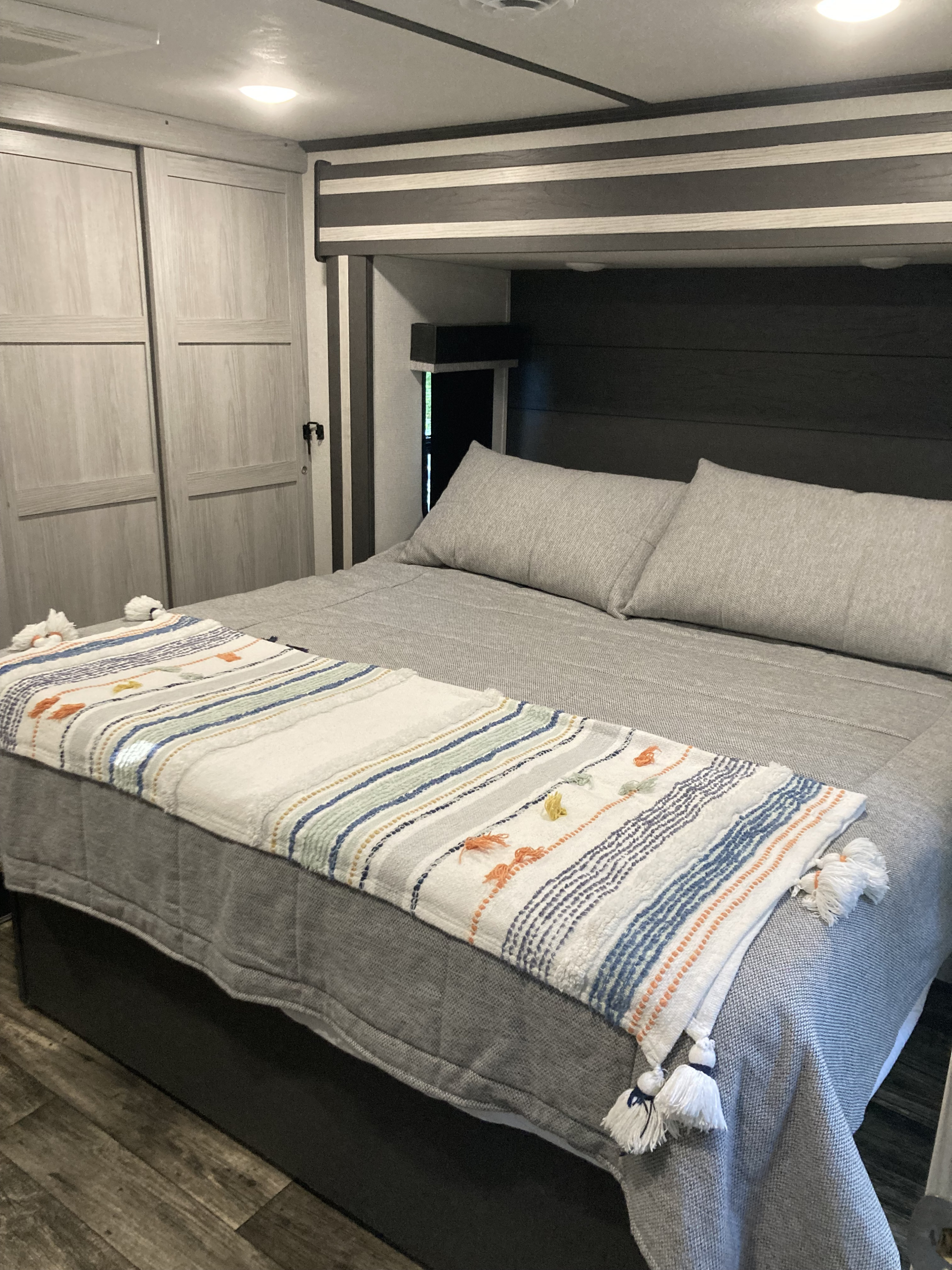 Cozy RV rental bedroom with grey bedding, a vibrant striped throw, ample storage, and wood-look flooring.. Keystone RV Fuzion 2023