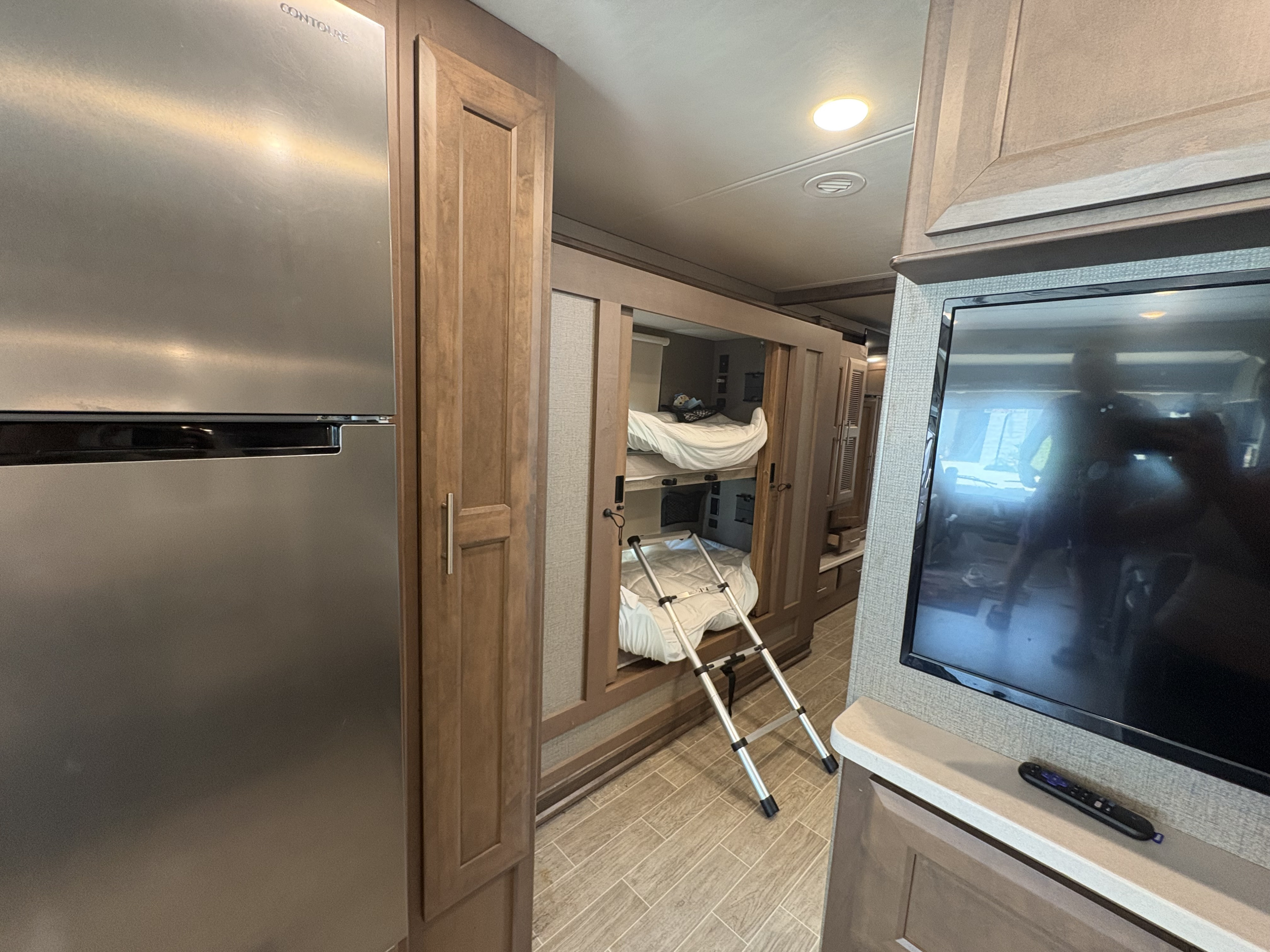 This spacious RV rental interior features a stainless steel refrigerator, built-in bunk beds with a ladder, and a TV.. Thor Miramar 2022