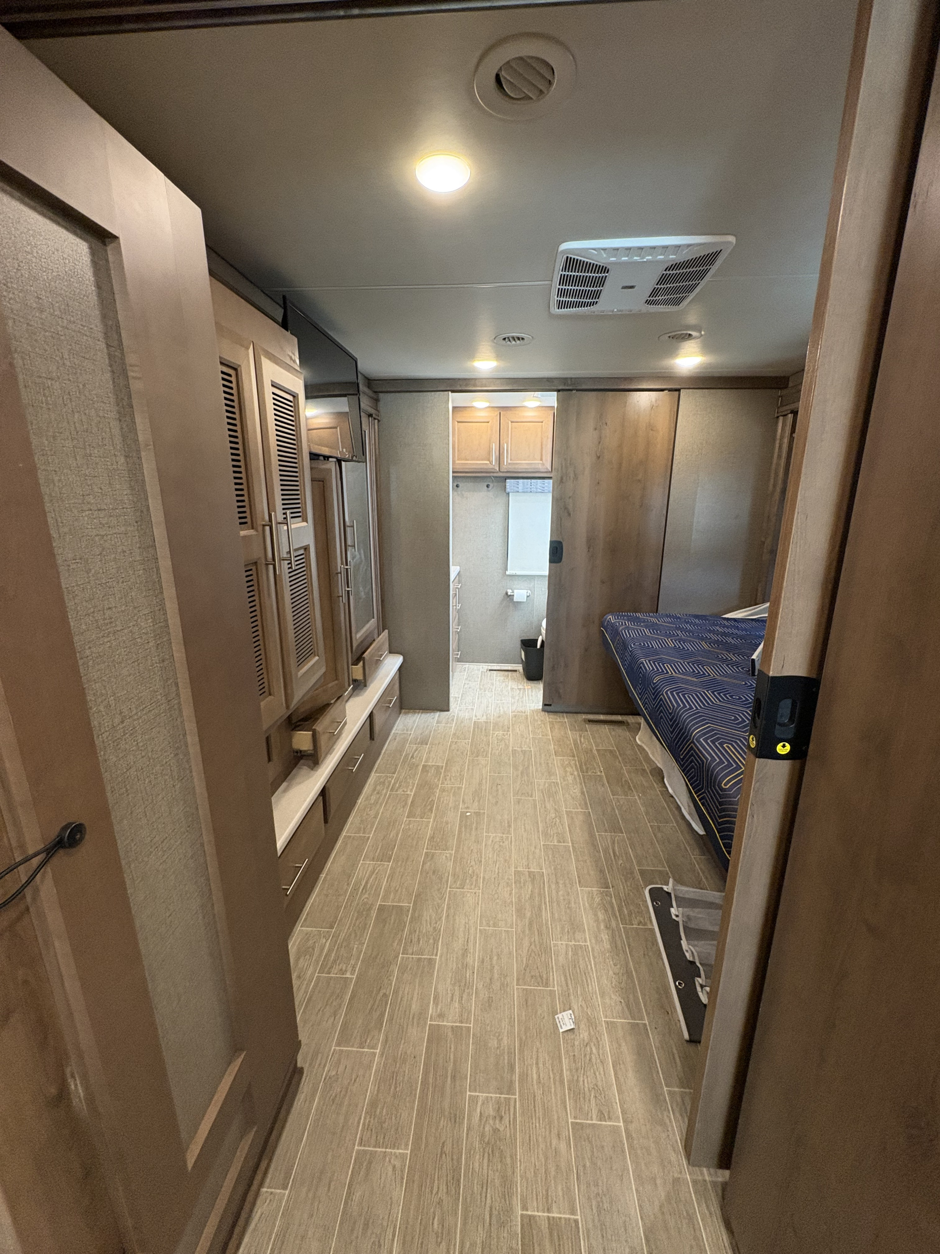RV rental interior: A bright hallway features wood cabinetry, leading to the bathroom. Bedroom with patterned bed visible on the right.. Thor Miramar 2022