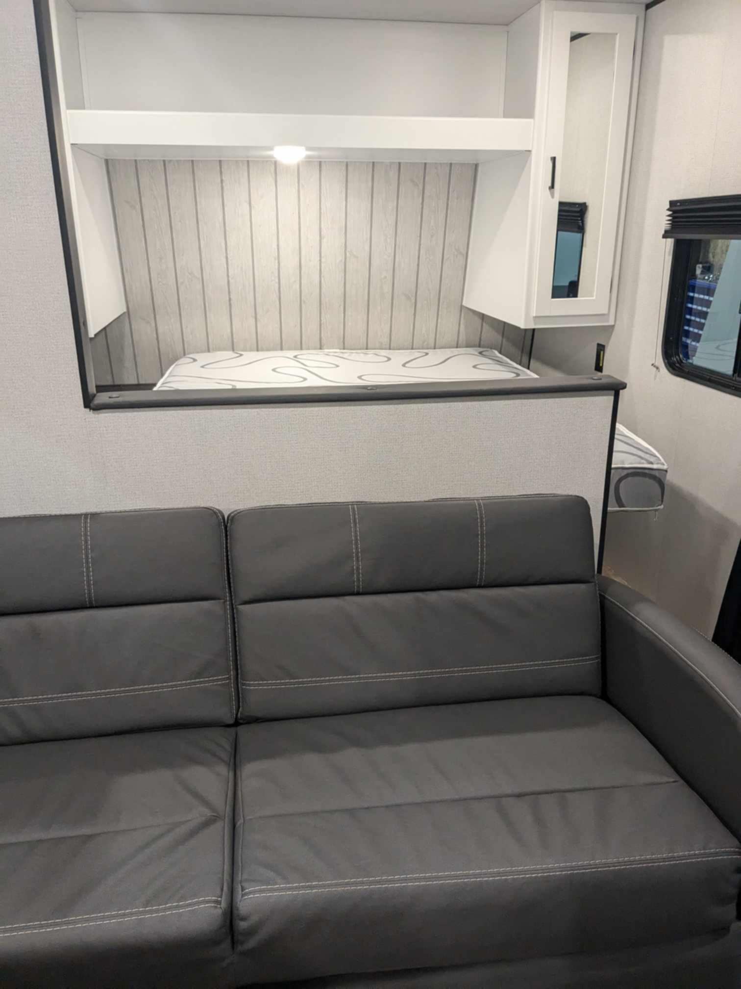 RV rental with a functional interior: gray sofa, elevated bed, and storage above.. Keystone RV Hideout Sport 2024