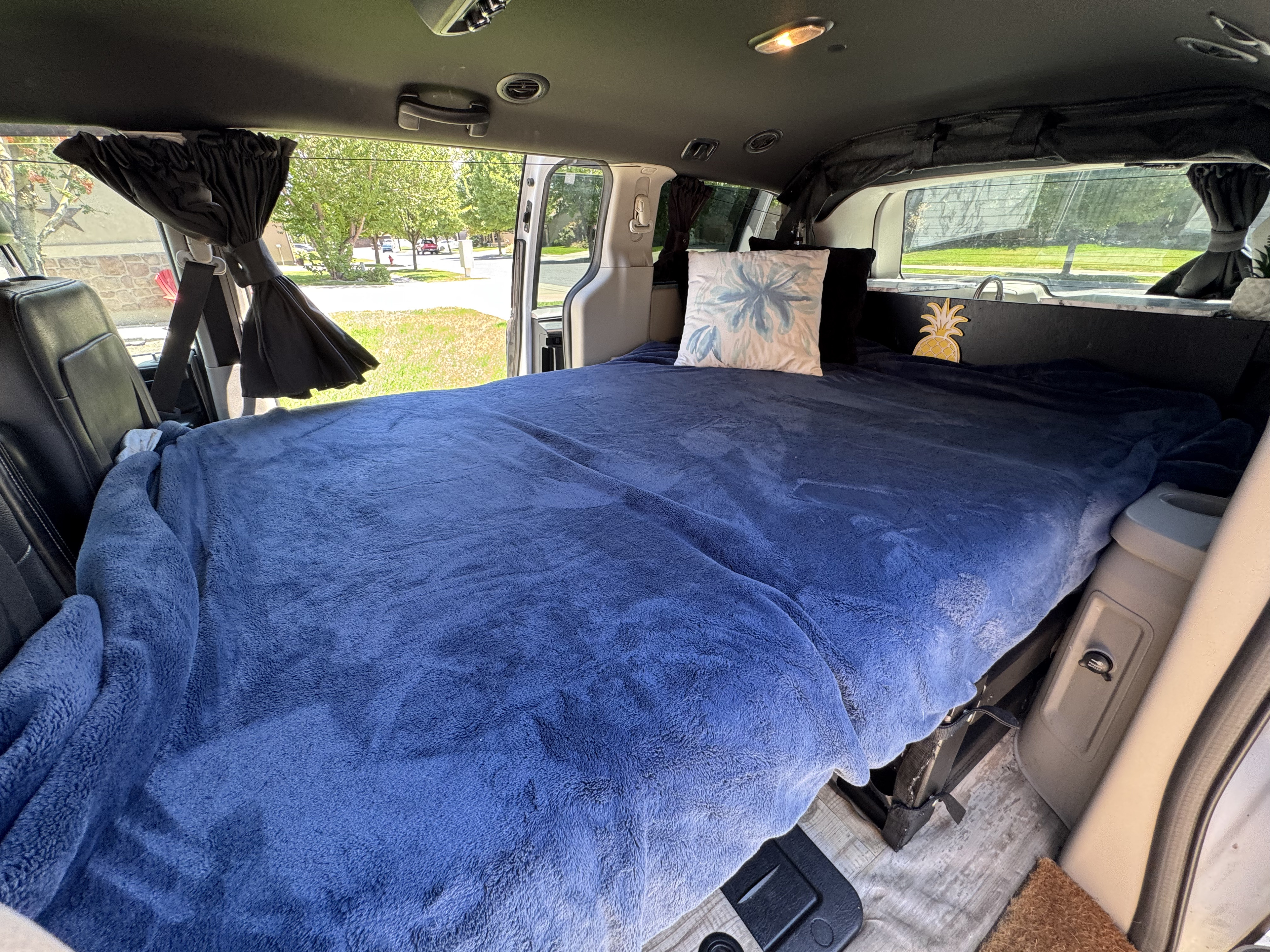 RV rental: Inside a converted camper van with a blue bed, privacy curtains, and a compact sink area.. Dodge Grand Caravan 2017
