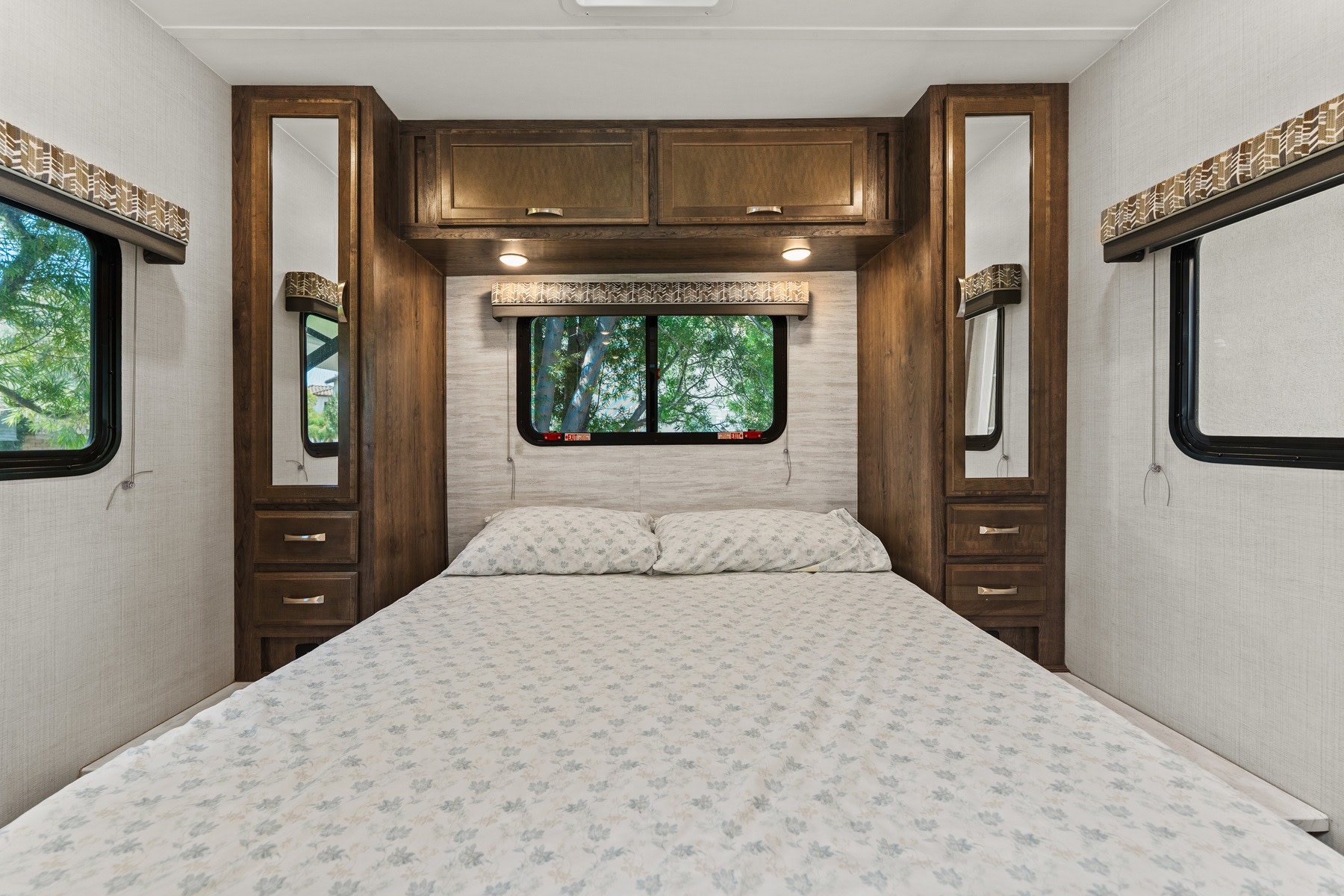 Cozy RV rental bedroom featuring a comfortable bed, window with nature views, and integrated wooden cabinets with mirrors.. Gulf Stream Conquest 2024