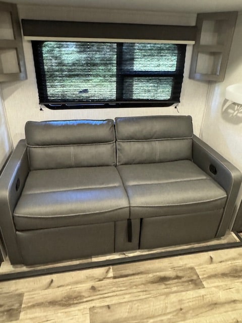 Spacious RV rental interior featuring a comfy gray sofa and large window with blinds, perfect for relaxing after adventures.. Keystone RV Coleman 1805RB 2022