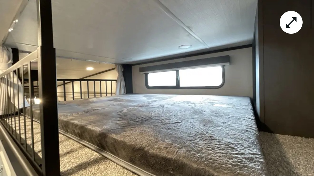 Cozy loft bed in an RV rental, featuring a wide grey bed, windows, and safety railing for comfortable travel.. Keystone Cougar 2025