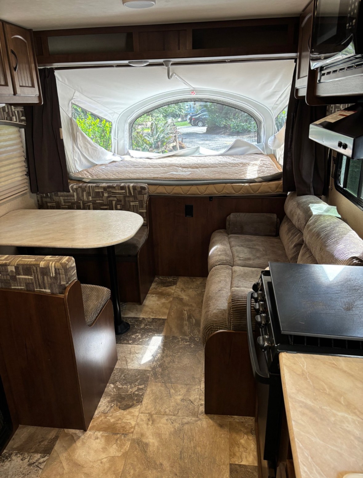 Bright RV rental interior featuring a pop-out bed with a scenic view, dinette, and lounge area. Ready for travel!. Jayco Jay Feather Ultra Lite 2015