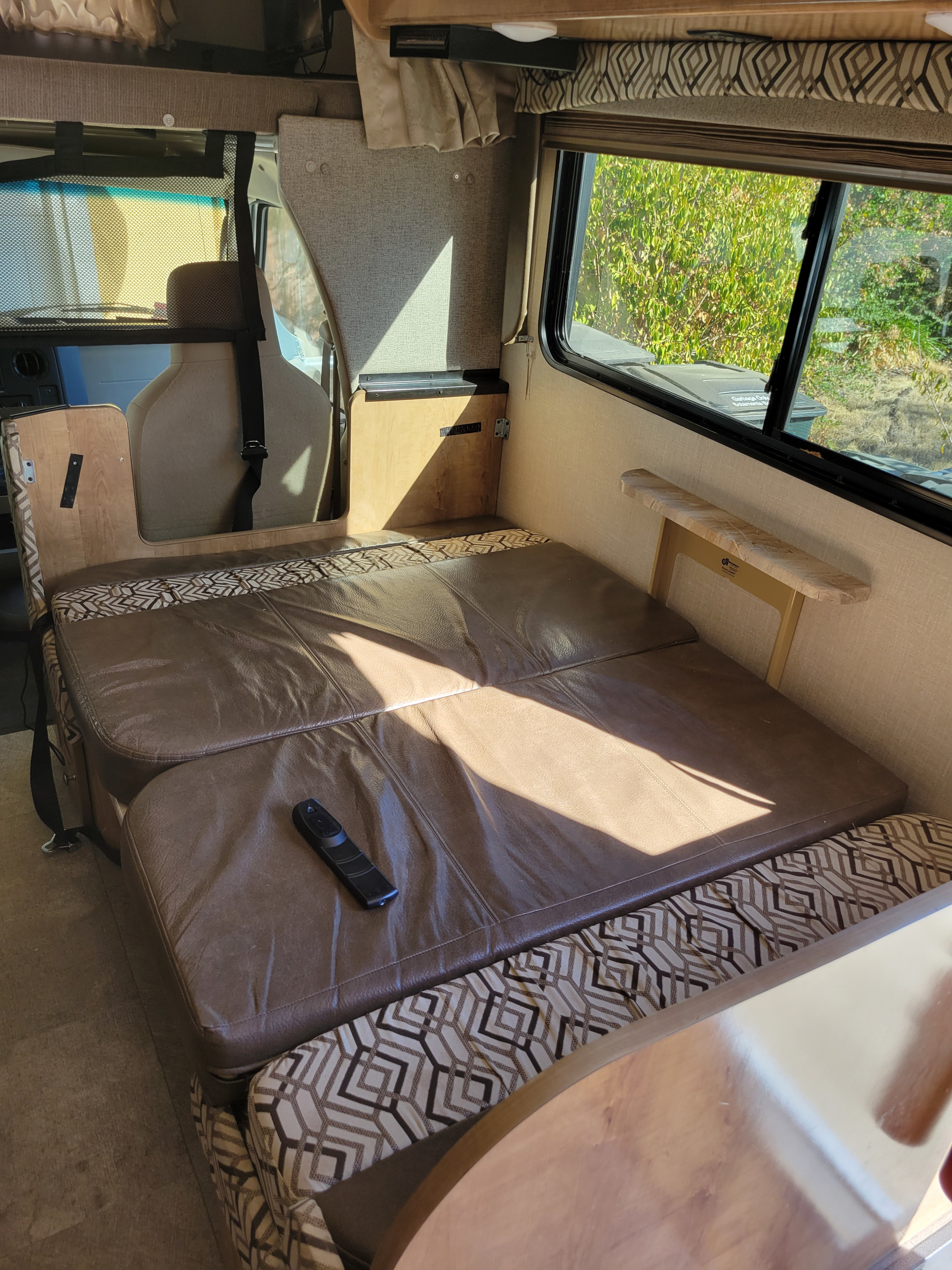 Inside an RV rental, showing a brown faux leather sofa converting to a bed, bathed in sunlight.. Coachman Leprechaun 2020