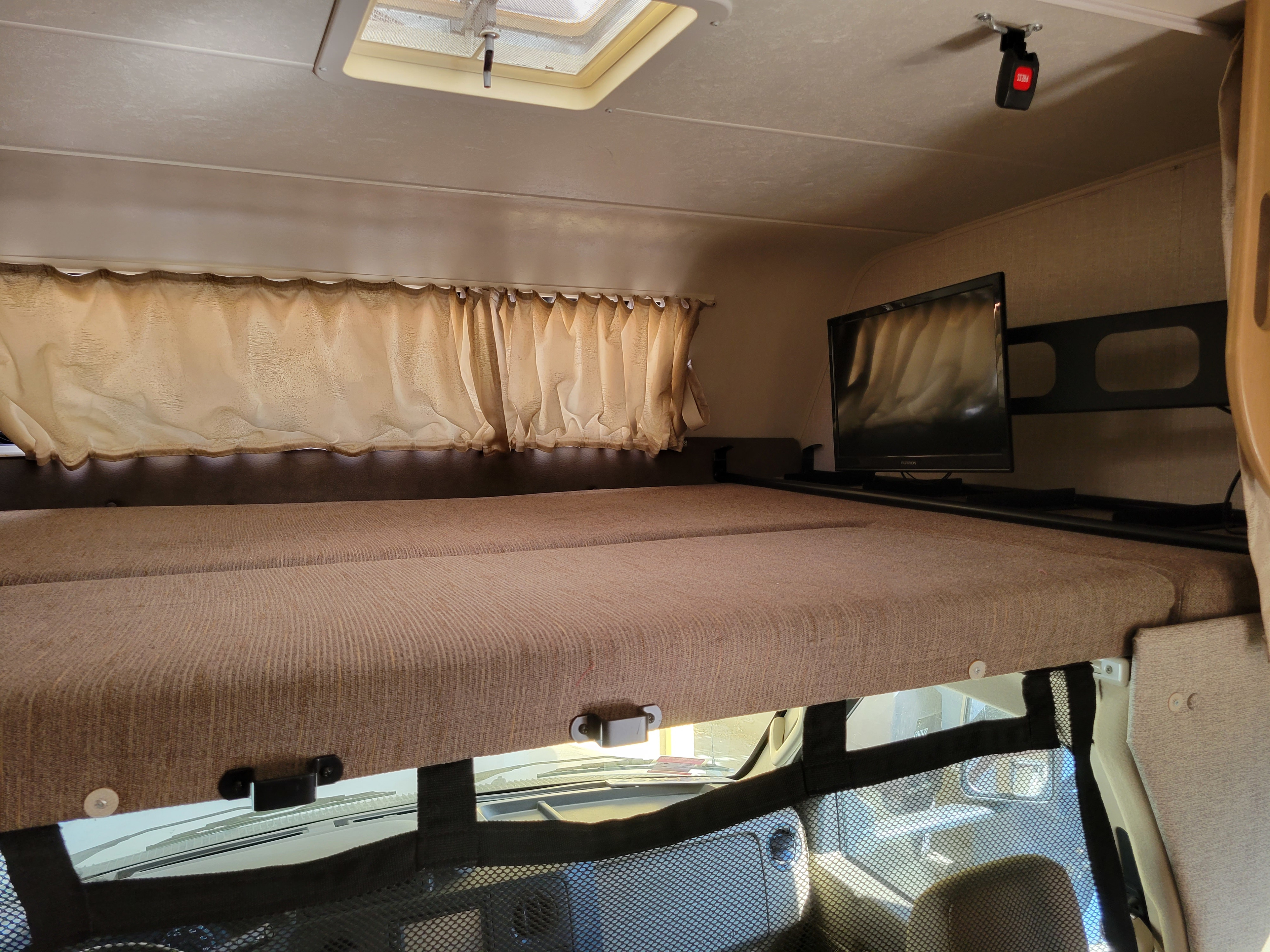 Cozy RV rental over-cab bunk bed with curtains, TV, and roof vent for your next adventure.. Coachman Leprechaun 2020
