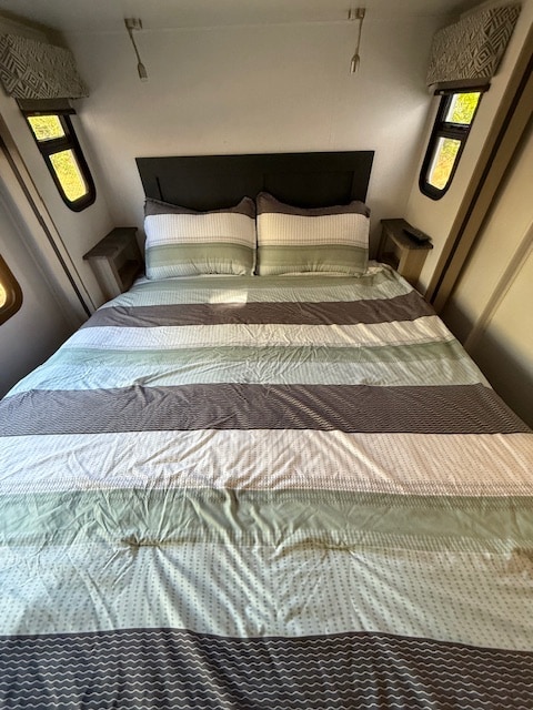 RV rental bedroom featuring a comfortable bed with green and grey striped comforter, built-in side tables, and windows.. Forest River Forester 2024