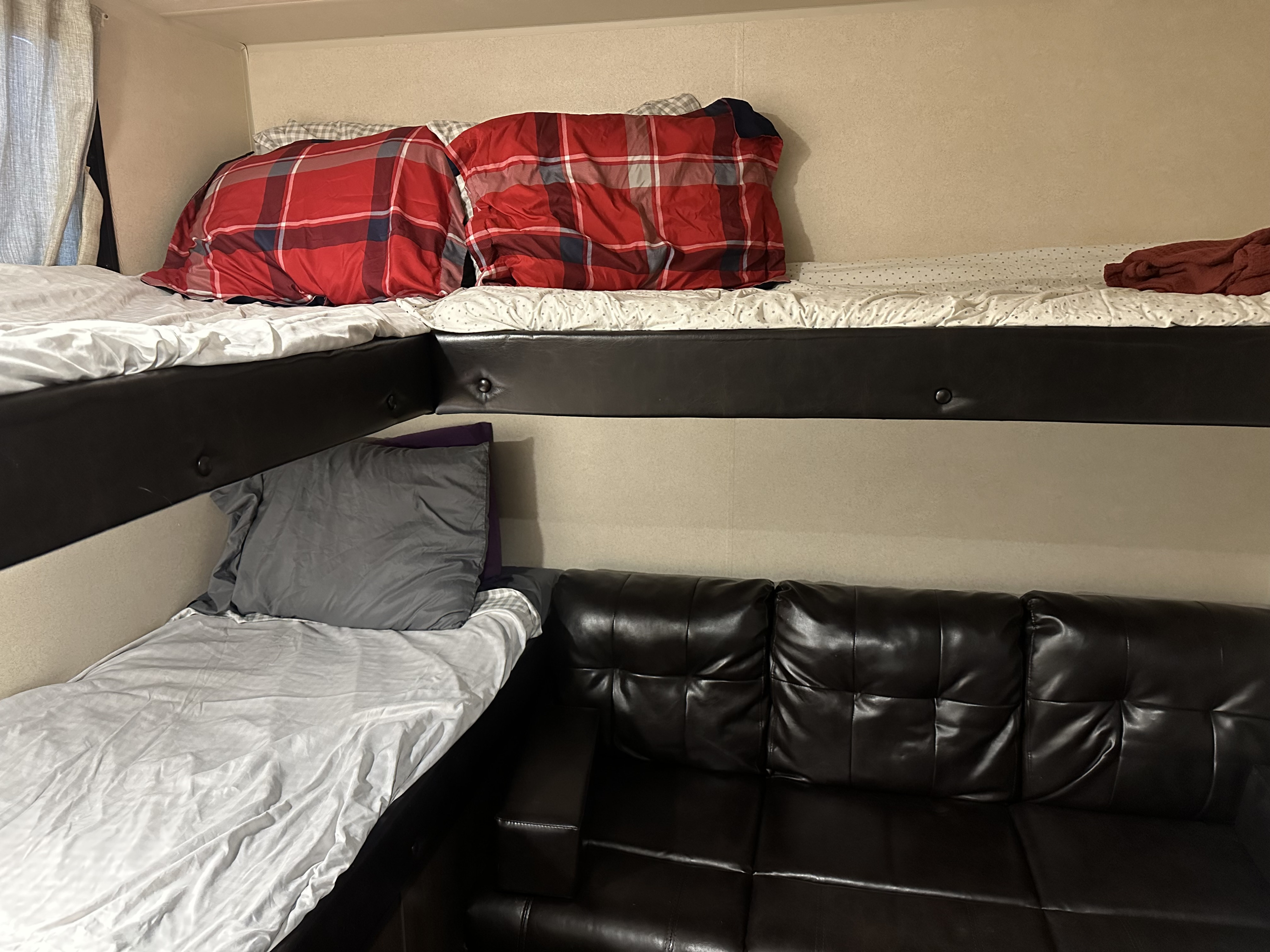 RV rental sleeping area showing stacked bunk beds with bedding and a black leather sofa below, ideal for family travel.. Forest River Wildwood X-Lite 2019