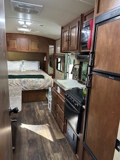 RV rental interior: A cozy bedroom, fully equipped kitchen with stove, sink, and refrigerator, all in warm wood finishes.. Forest River Surveyor Cadet 2014
