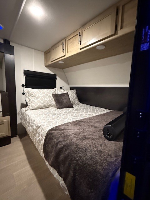 Cozy RV rental bedroom featuring a comfortable bed with patterned bedding, overhead cabinets, and modern interior design.. Forest River Cherokee Wolf Pup 2026