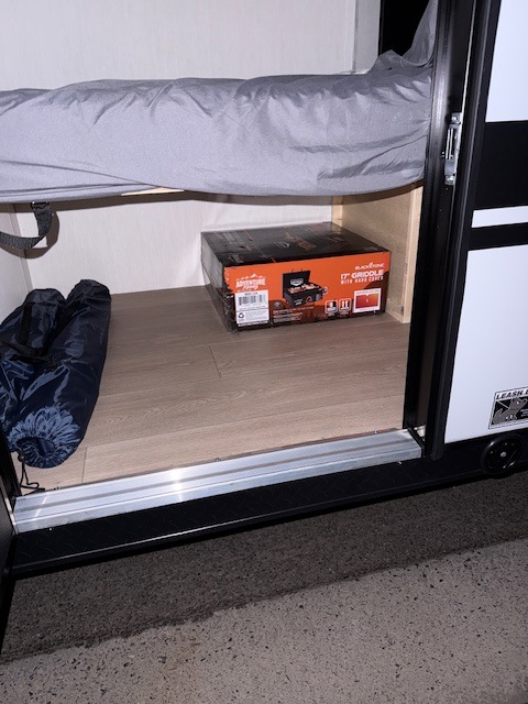 Under-bed storage in an RV rental shows a Blackstone griddle box and rolled sleeping bags on wood flooring.. Forest River Cherokee Wolf Pup 2026