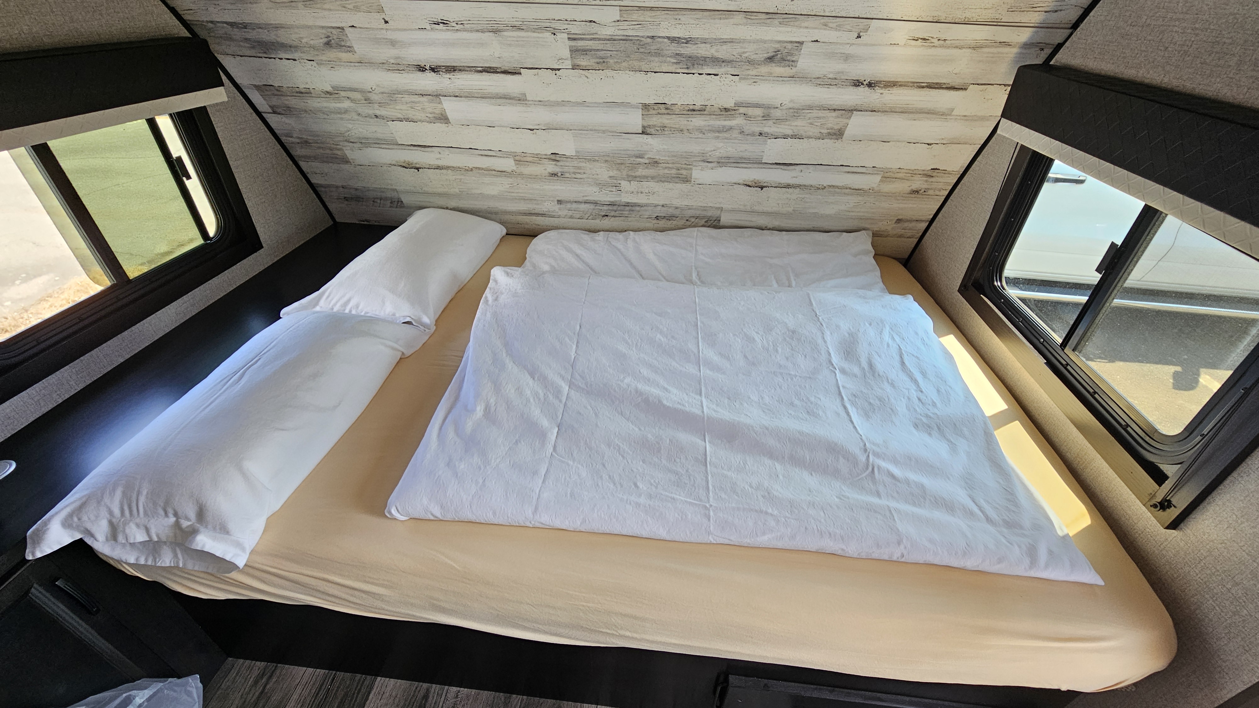 Cozy RV rental bedroom featuring a comfy bed with a light sheet and white duvet, flanked by two large windows.. Jayco Jay Feather 2020