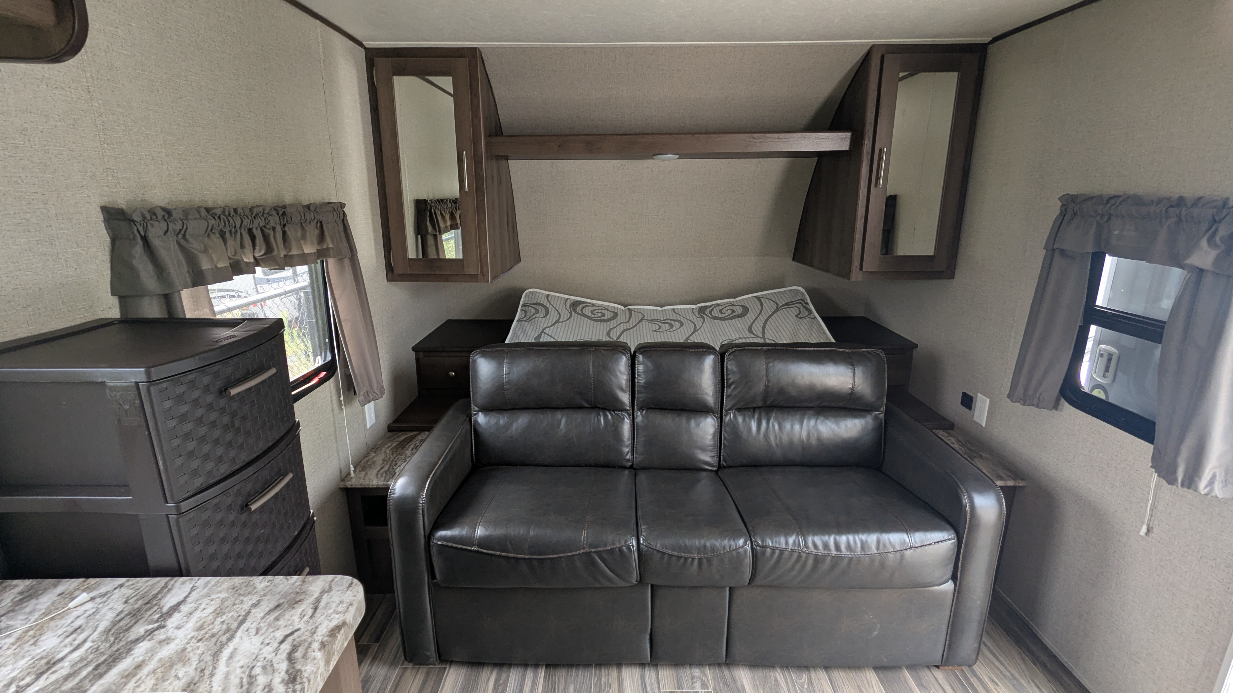 Comfortable RV living space with dark leather sofa, bed, cabinets, and draped windows, ideal for an RV rental.. Forest River Shasta 2020