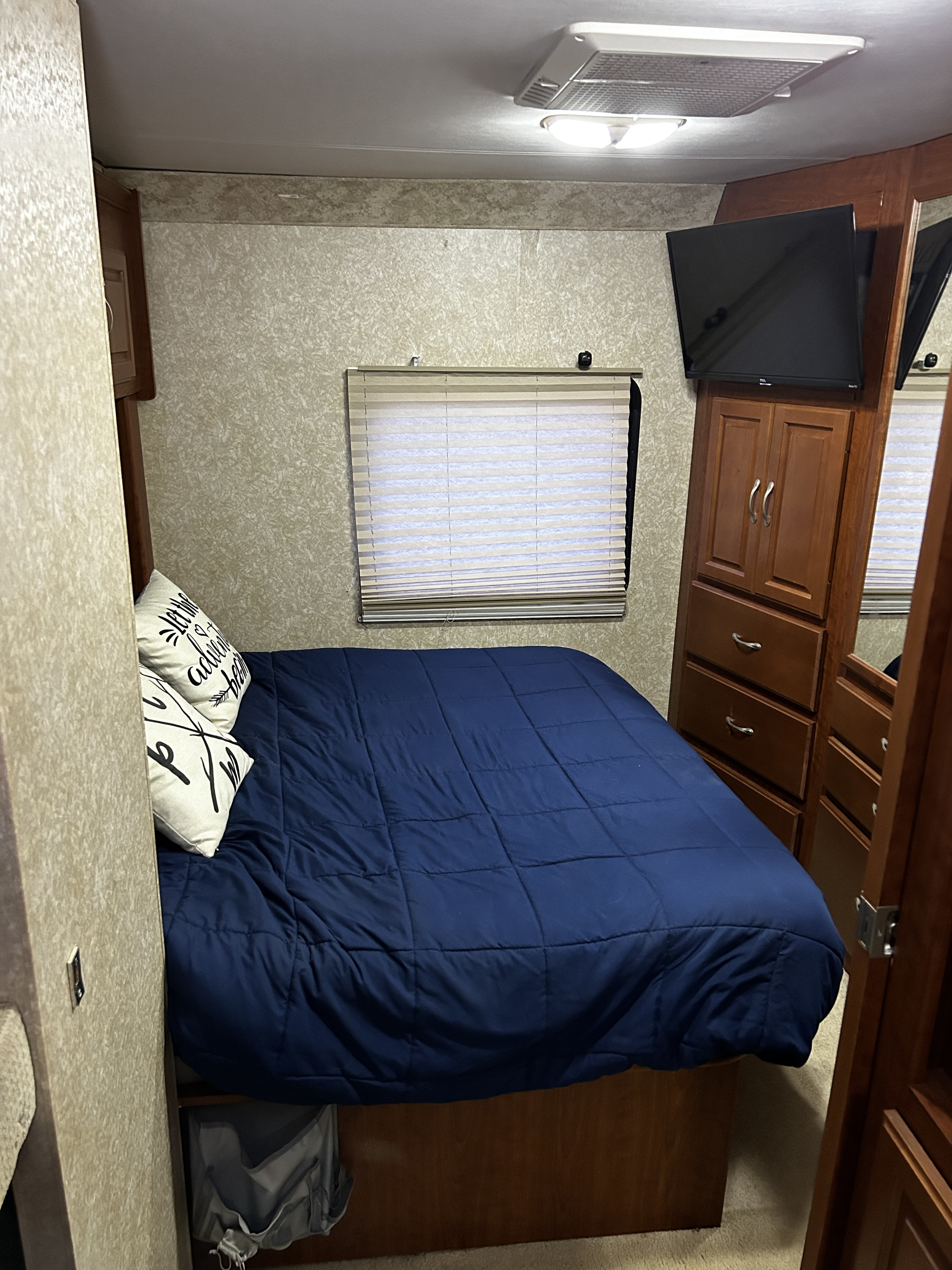 Cozy RV rental bedroom featuring a blue bed, window with blinds, TV, and built-in storage. Ideal for comfortable travel.. Dutchmen Kodiak 2007