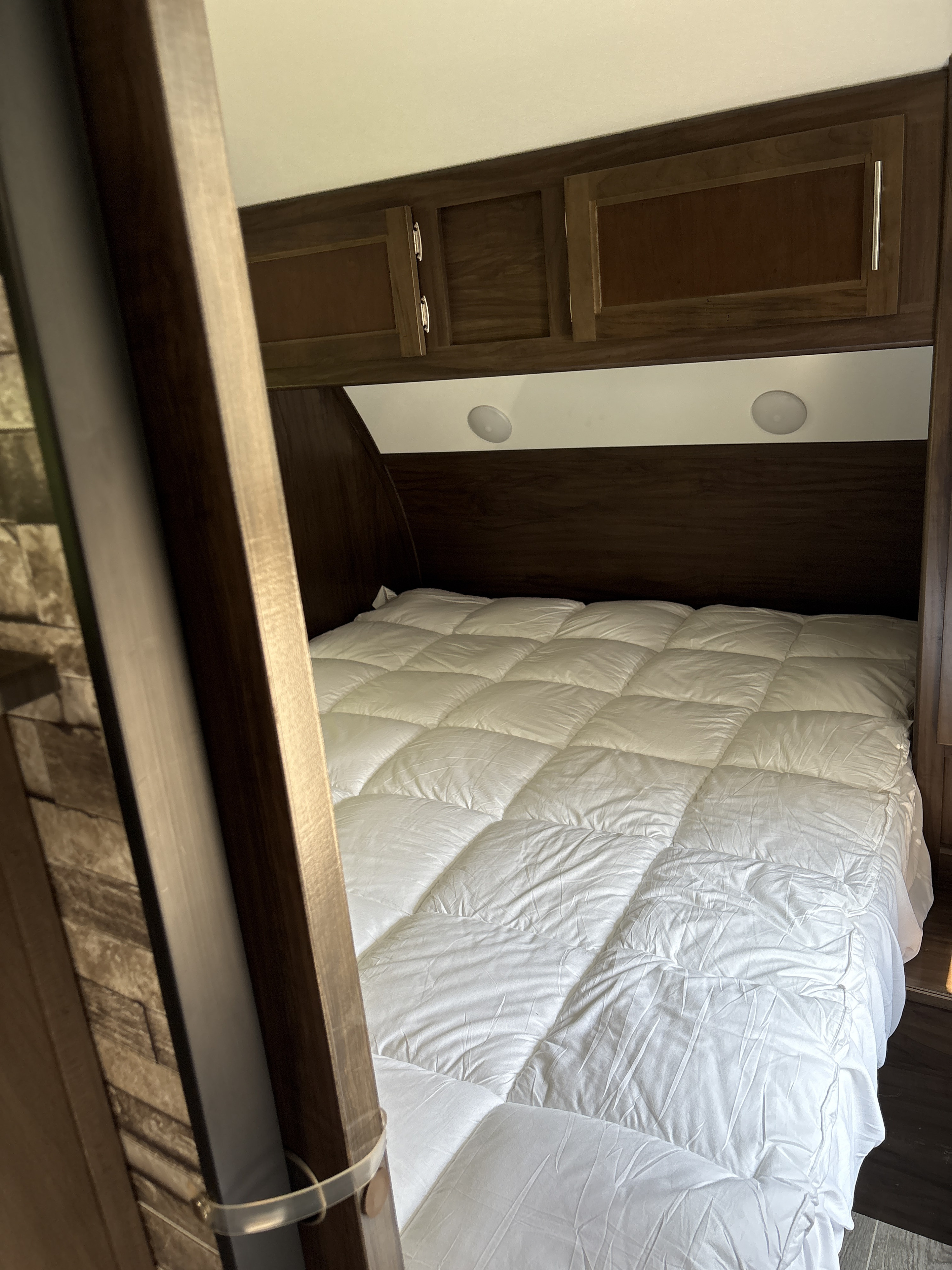 Cozy RV rental bedroom featuring a comfy bed with white comforter, overhead storage, and lights.. Forest River Cherokee Grey Wolf 2019