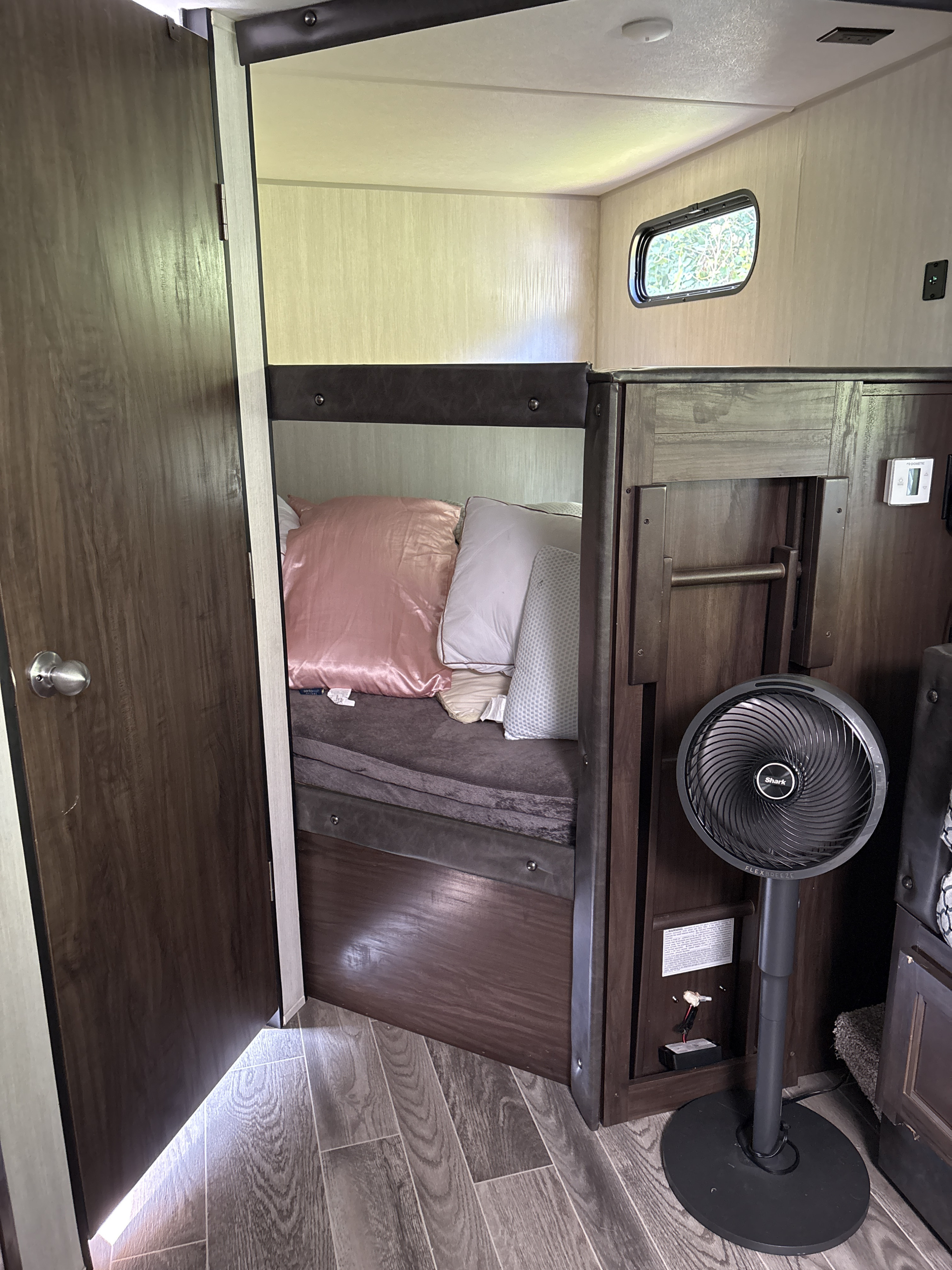 Inside an RV rental: a compact sleeping area with bunk beds, a partially open door, and a standing fan.. Forest River Cherokee Grey Wolf 2019