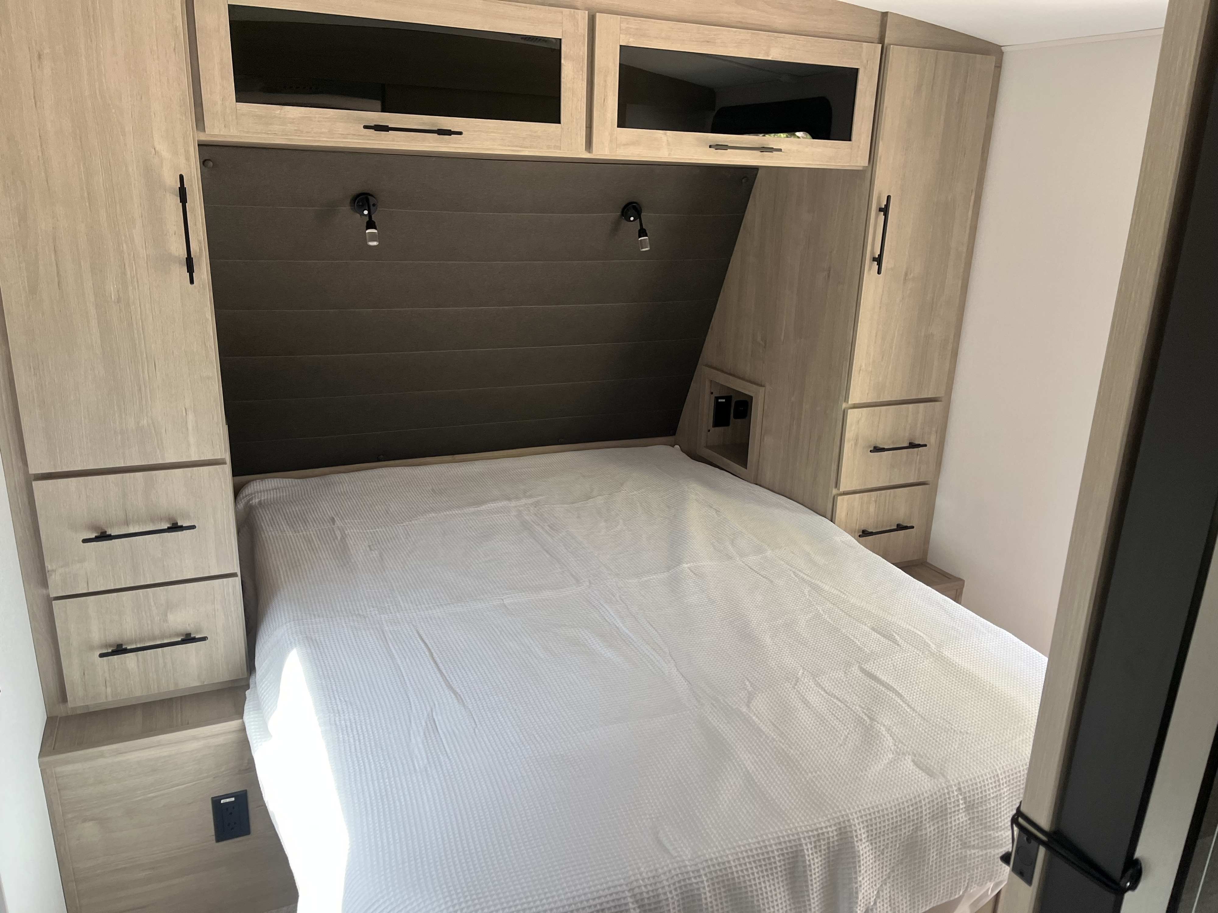Comfortable RV rental bedroom featuring a bed with white bedding, modern light wood cabinets, reading lights, and built-in storage.. Grand Design 2800BH 2025