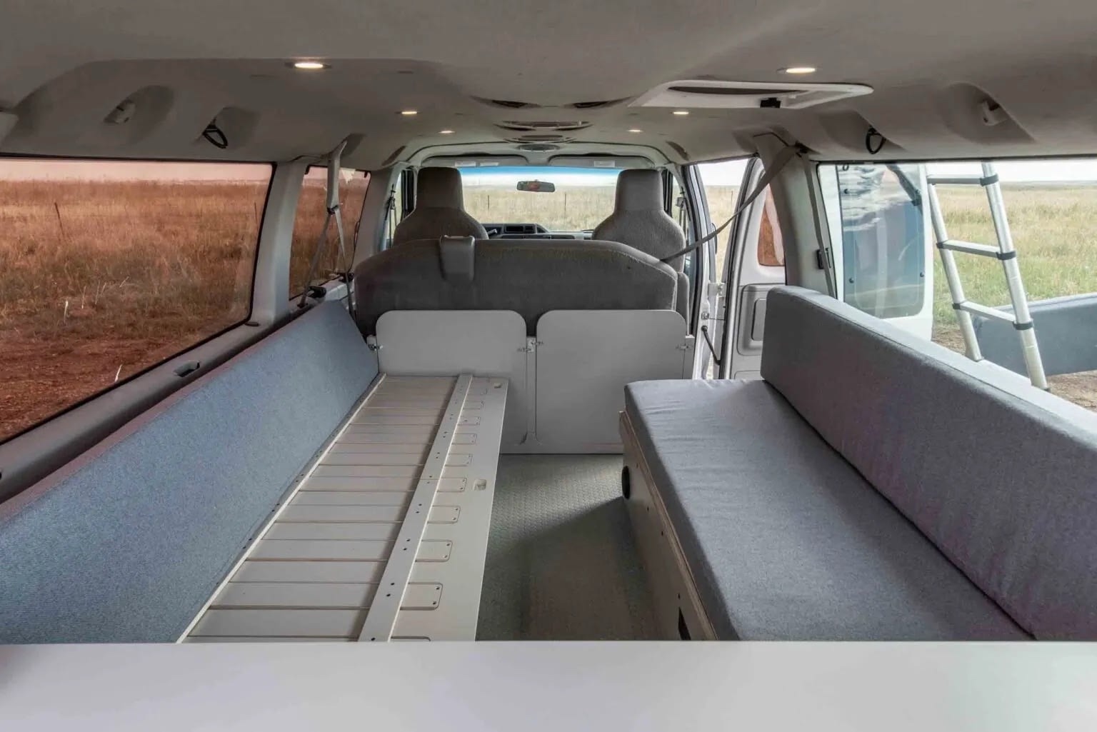 Explore this RV rental's spacious interior: grey cushioned beds/seating, a central platform, and scenic views from the open back door.. Ford Econoline 2014