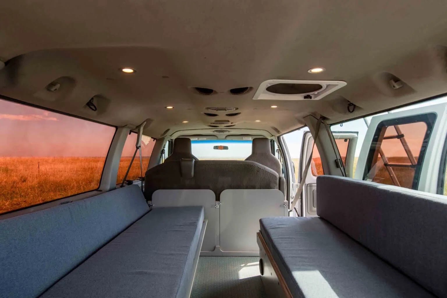 Inside a spacious RV rental campervan, featuring convertible beds & a view of a vast, golden field. Perfect for road trips!. Ford Econoline 2014