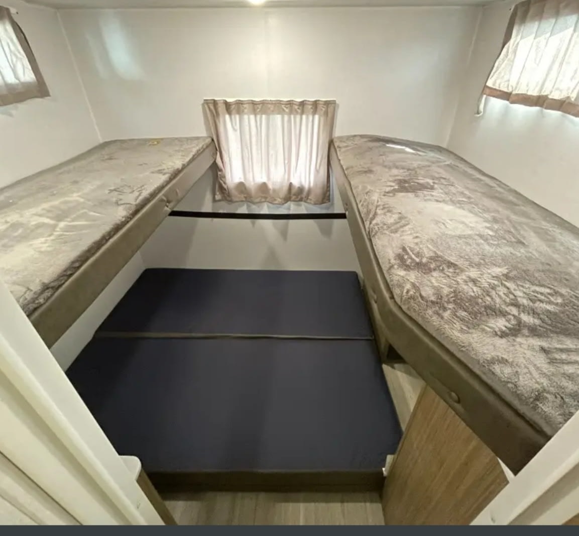 Inside an RV rental: versatile sleeping space with two elevated bunk beds and a convertible floor bed below small windows.. Forest River Wildwood X-Lite 28VBXLX 2025