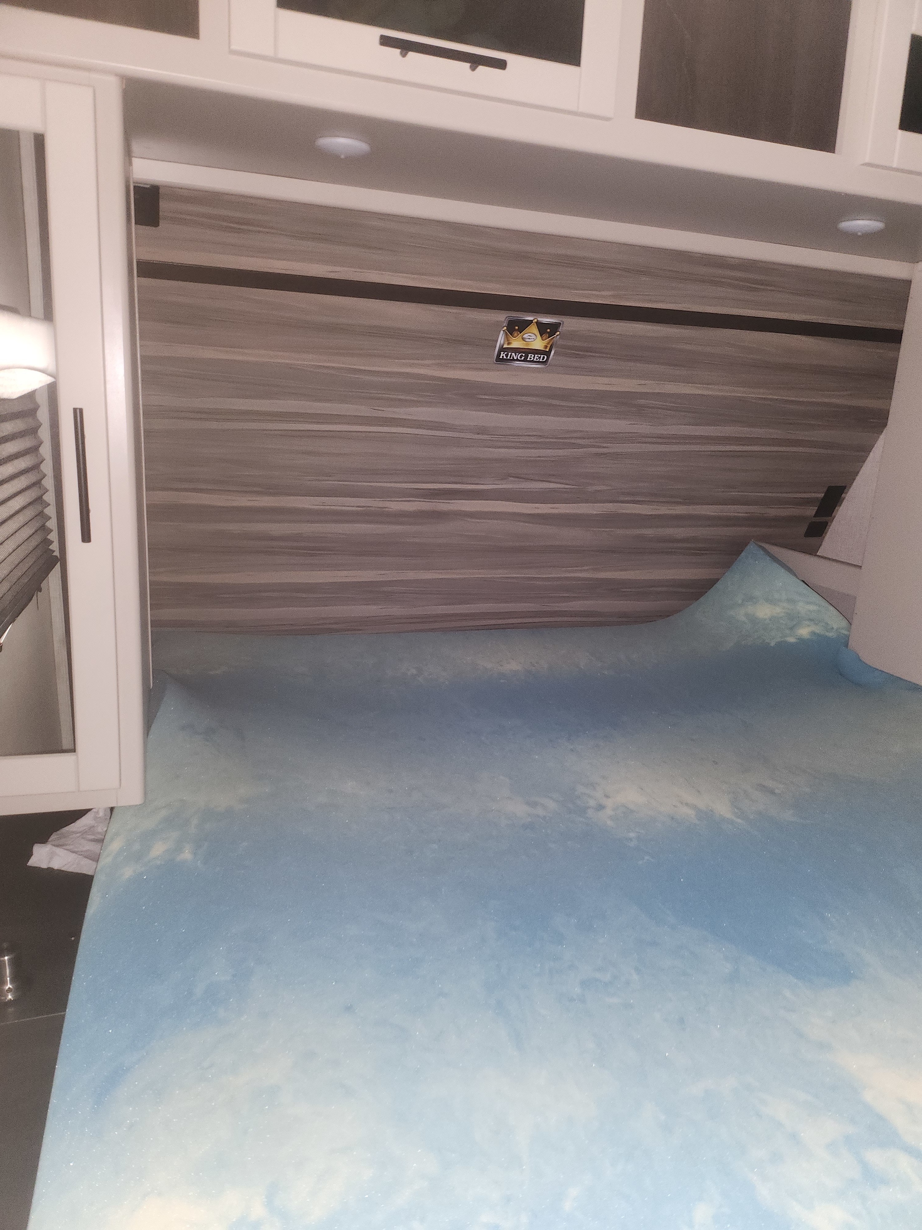 Spacious king bed with a blue foam mattress topper in an RV rental, complete with overhead cabinets and wood paneling.. Crossroads RV Cruiser Aire 2021