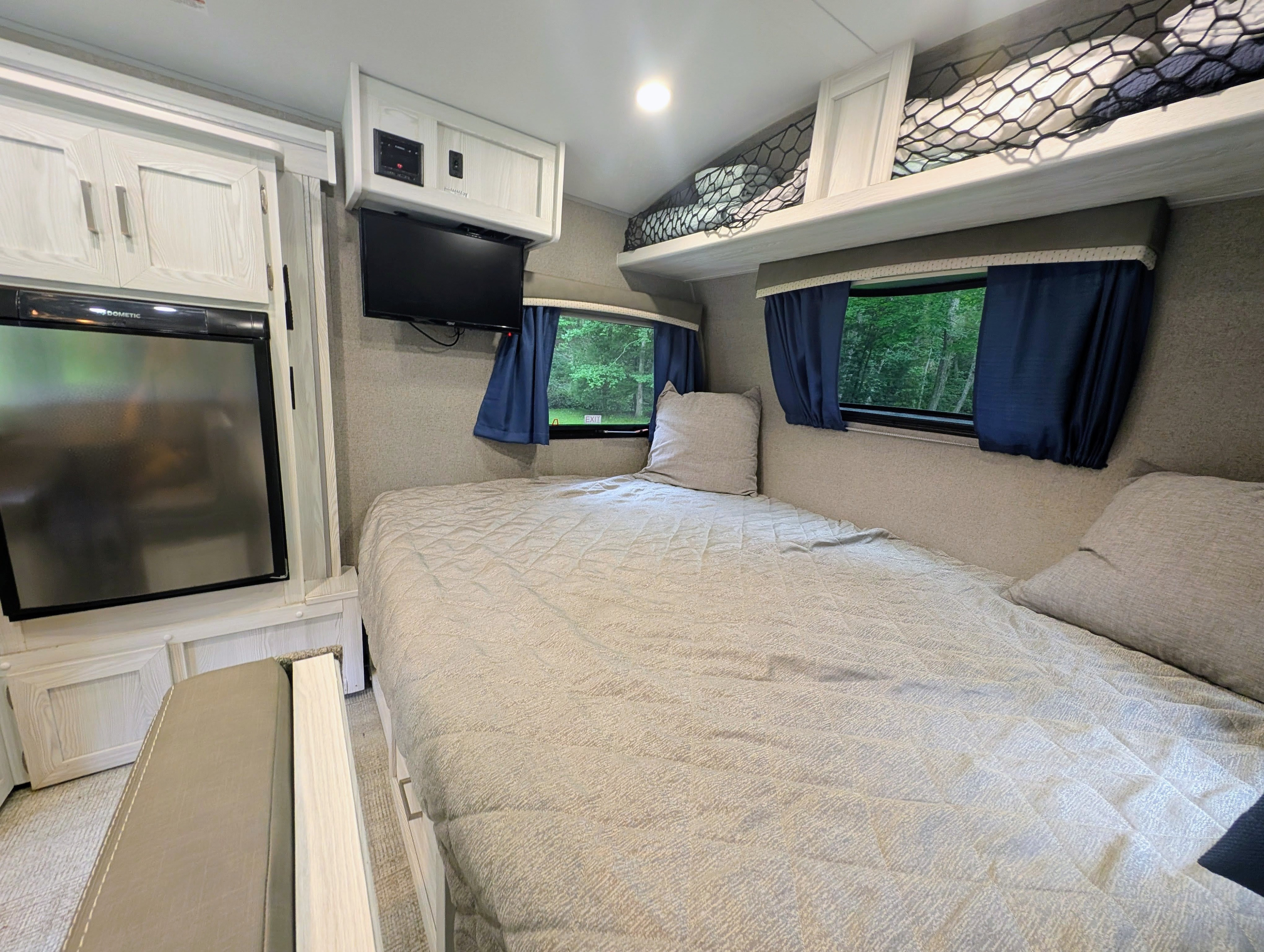 Cozy RV rental bedroom featuring a comfortable bed, overhead bunk, TV, refrigerator, and scenic window views.. Fleetwood Rockwood 2021