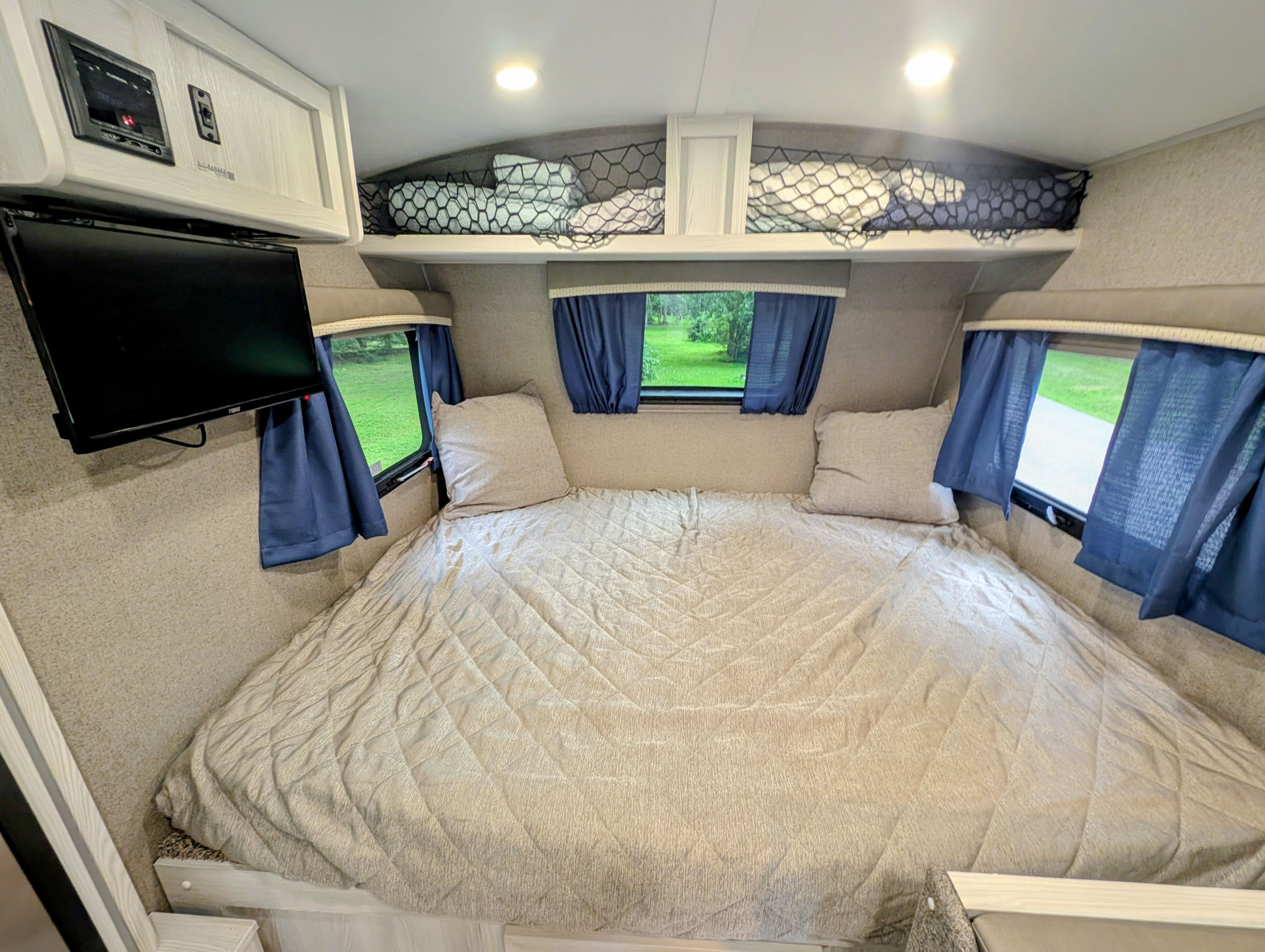 Comfy RV rental bedroom with a large bed, windows with blue curtains, TV, and overhead storage for a cozy trip.. Fleetwood Rockwood 2021