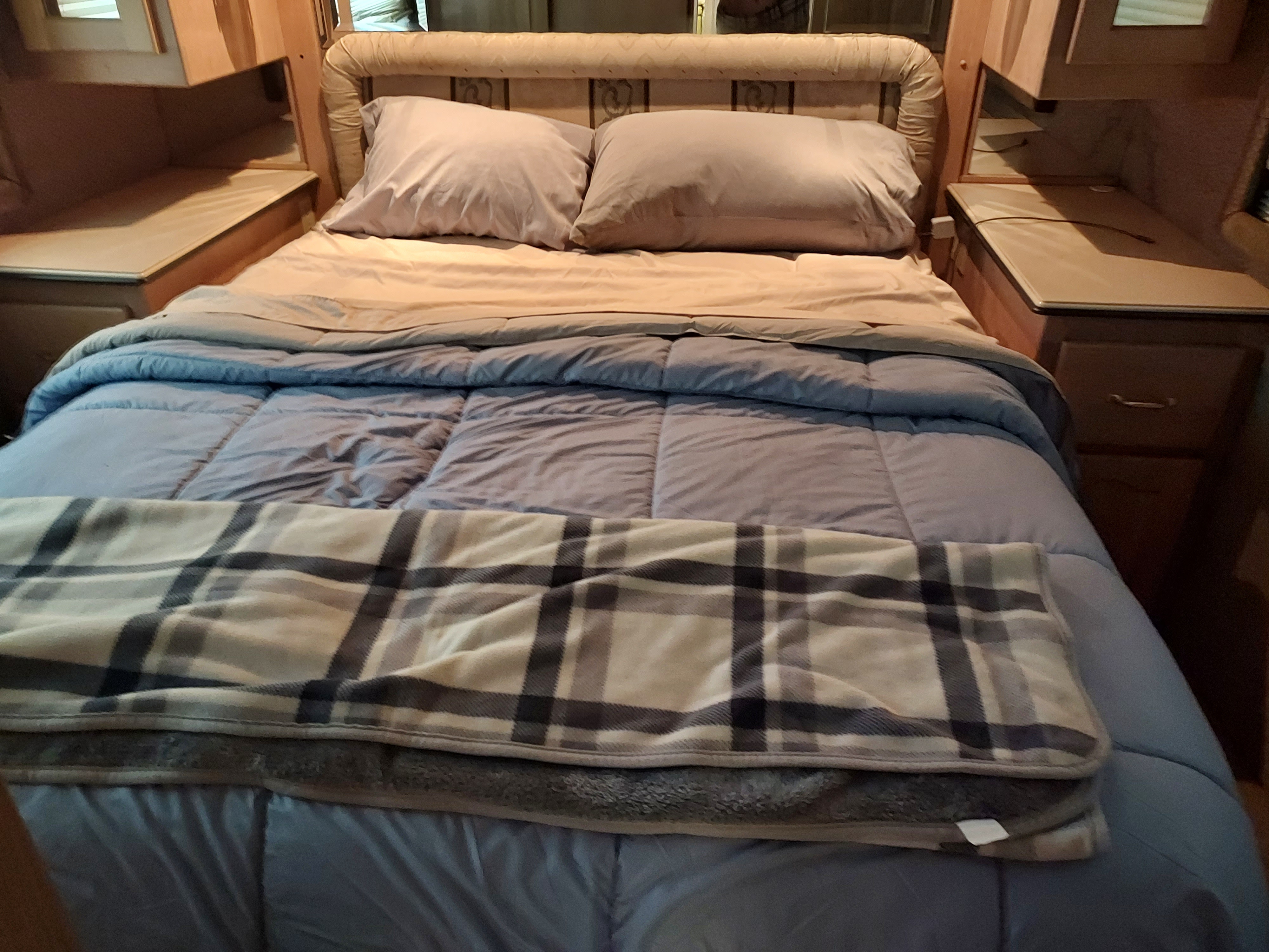 Step into comfort: a cozy RV rental bedroom featuring a neat bed with blue comforter and plaid blanket.. Beaver Patriot Ticonderoga 2000