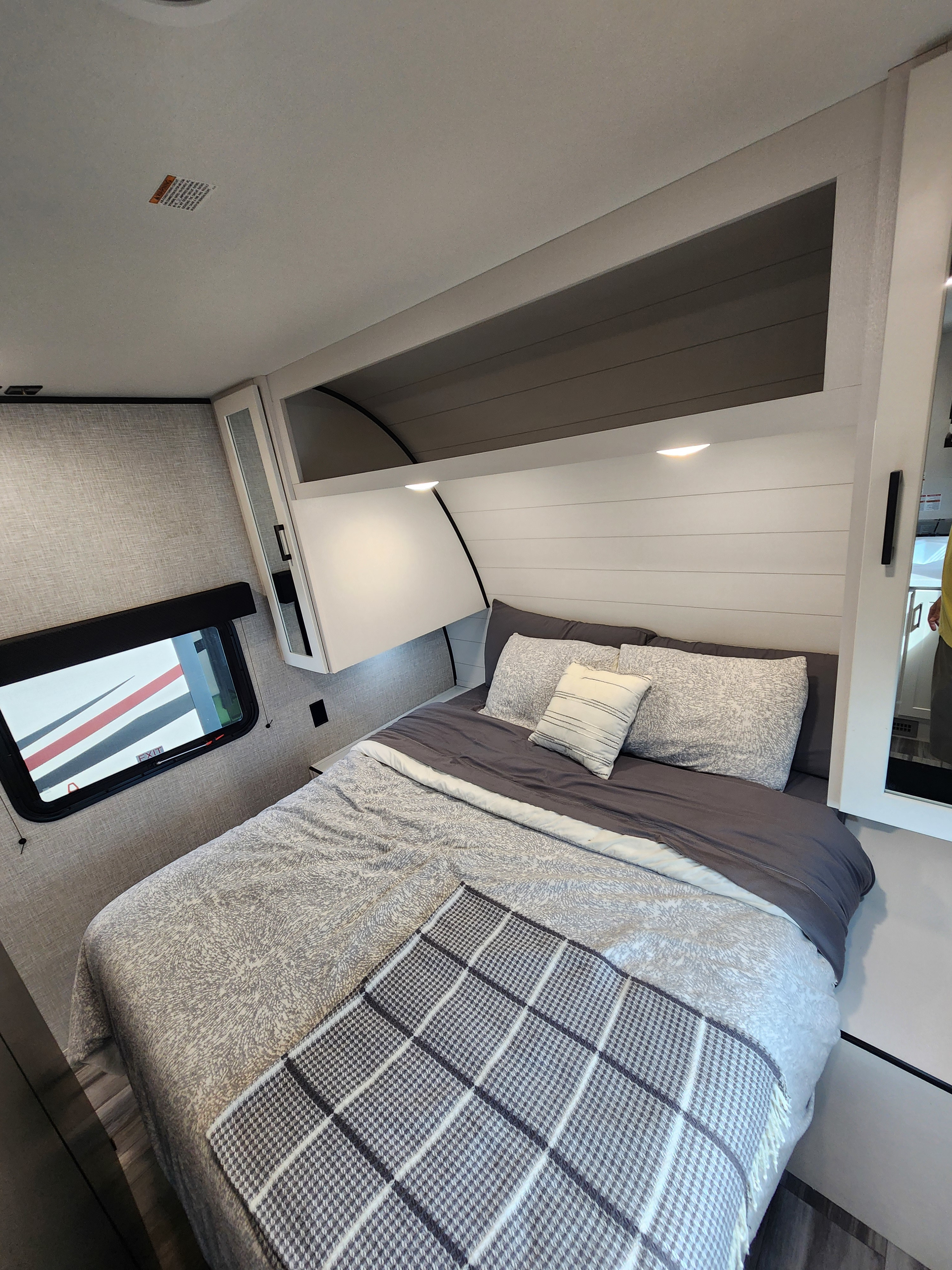 Cozy RV rental bedroom with a large bed, grey bedding, sleek overhead cabinets with lights, and a side window for scenic views.. Jayco Jay Flight SLX 2024