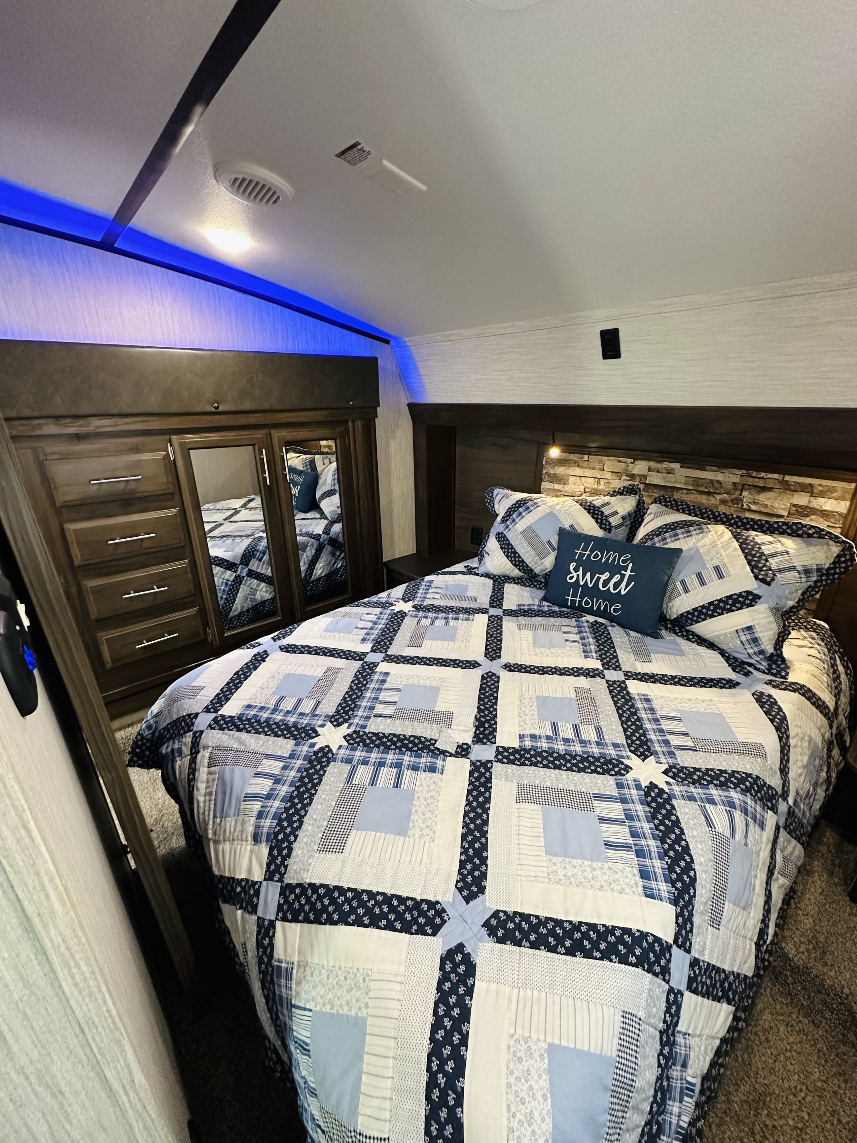 Comfortable RV rental bedroom with blue quilt, wooden storage, and ambient lighting, creating a cozy home-like interior.. Forest River Cherokee Arctic Wolf 2019