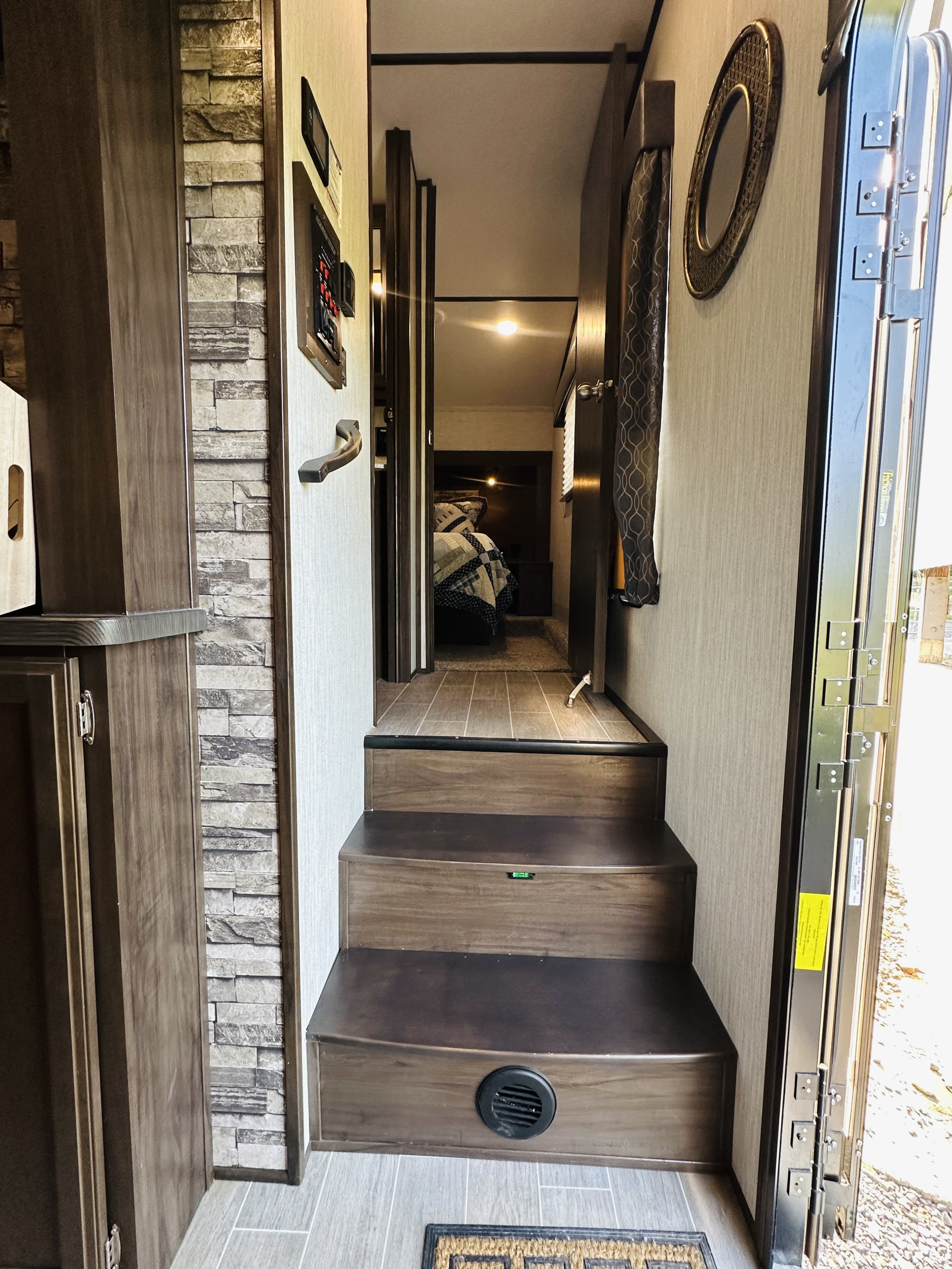 Inside an RV rental, wood-look steps descend to the tiled floor, leading to a hallway and a cozy bedroom.. Forest River Cherokee Arctic Wolf 2019