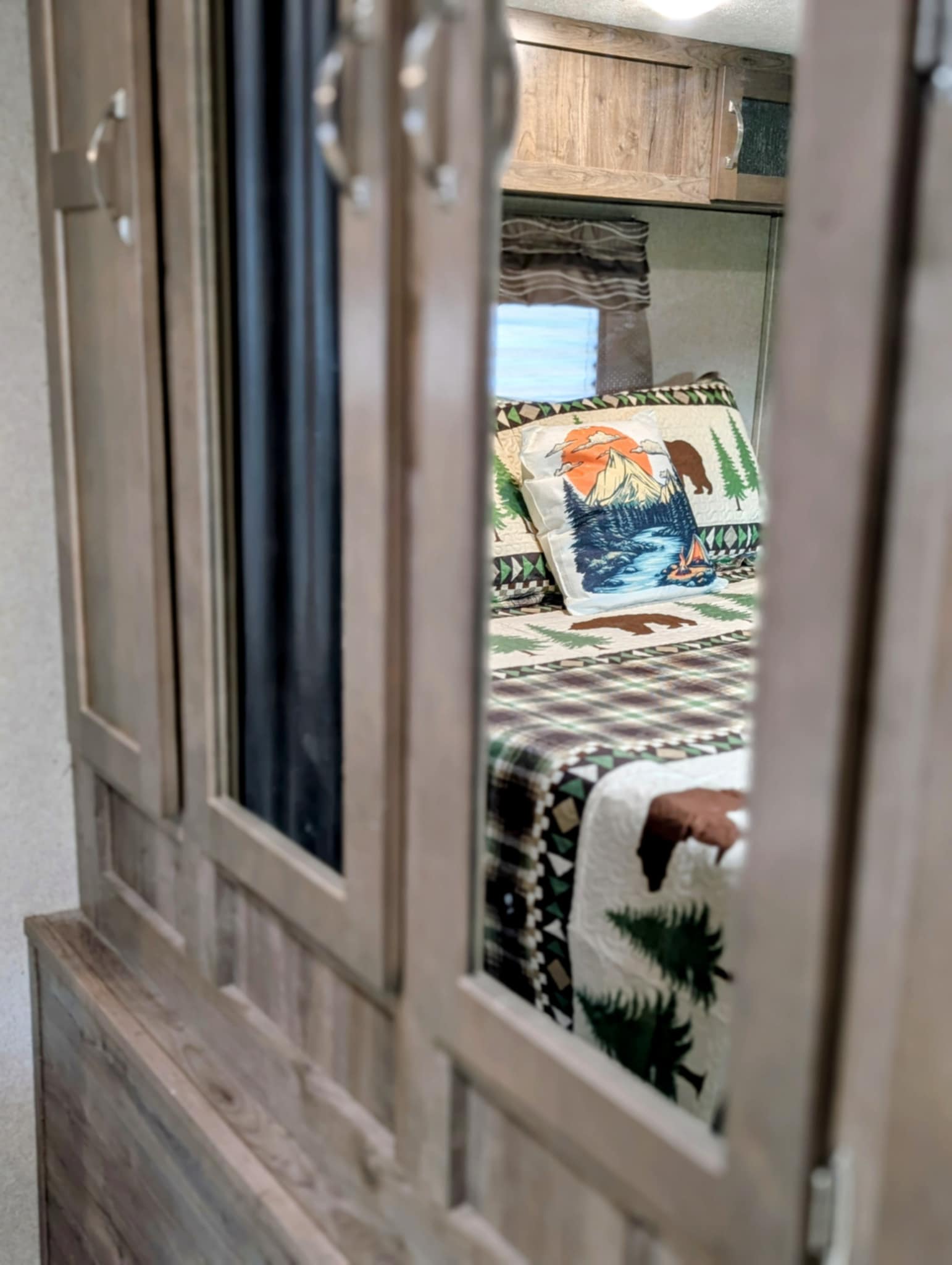 RV rental bedroom: cozy, nature-themed bedding and wooden cabinets reflected in mirrored doors.. Palomino Puma 32RBFQ 2019