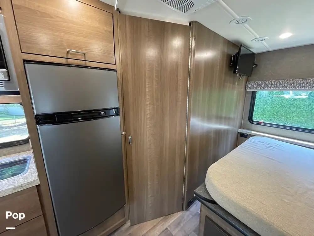 This RV rental's interior features a modern silver fridge, wood-grain cabinets, and a comfortable sleeping area with a TV.. Pulse Pulse Motorhome 2018