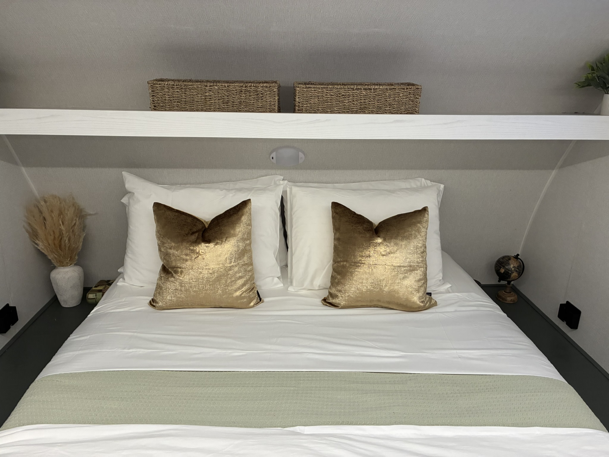 Cozy RV rental bedroom featuring a comfy bed with white linens, gold pillows, a shelf with baskets, and decorative accents.. Heartland RVs Eddie Bauer Edition 17RB-C 2025