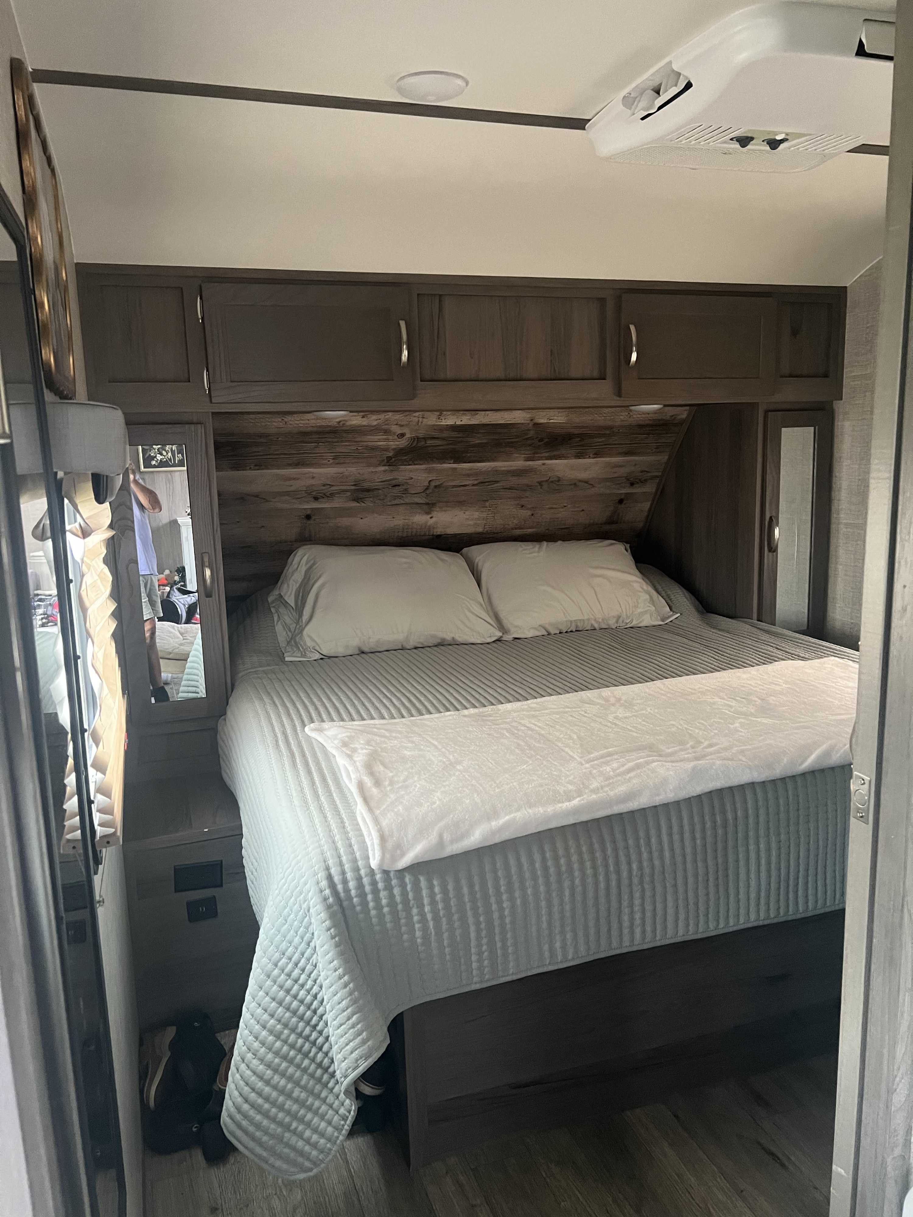 Relax in this inviting RV rental bedroom featuring a comfy bed, rustic headboard, overhead storage, and mirrored closets.. Gulf Stream Envision 2021
