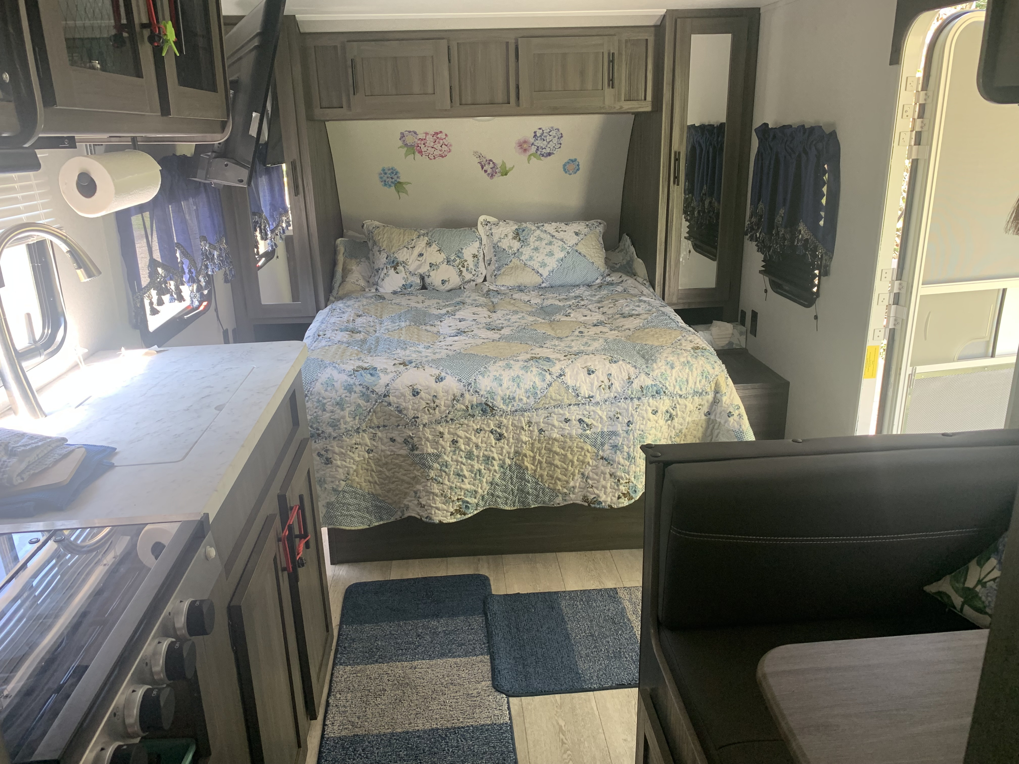 Cozy RV rental interior: kitchen with sink & stove, comfy bed with floral quilt, and dining area. Perfect for your next adventure!. Forest River Shasta 2021