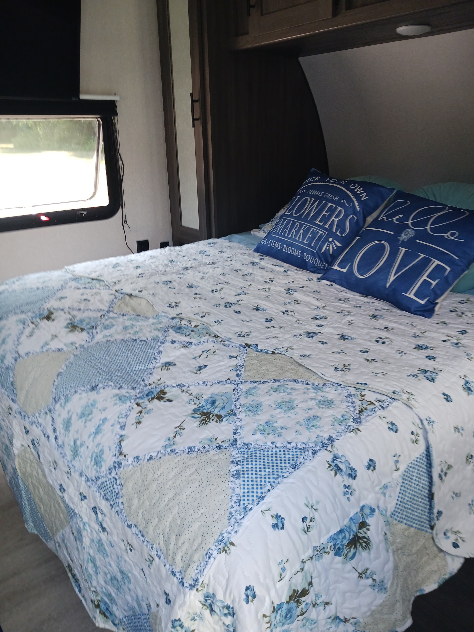 Cozy RV rental bedroom featuring a bed with a blue and white floral quilt and decorative pillows.. Forest River Shasta 2021