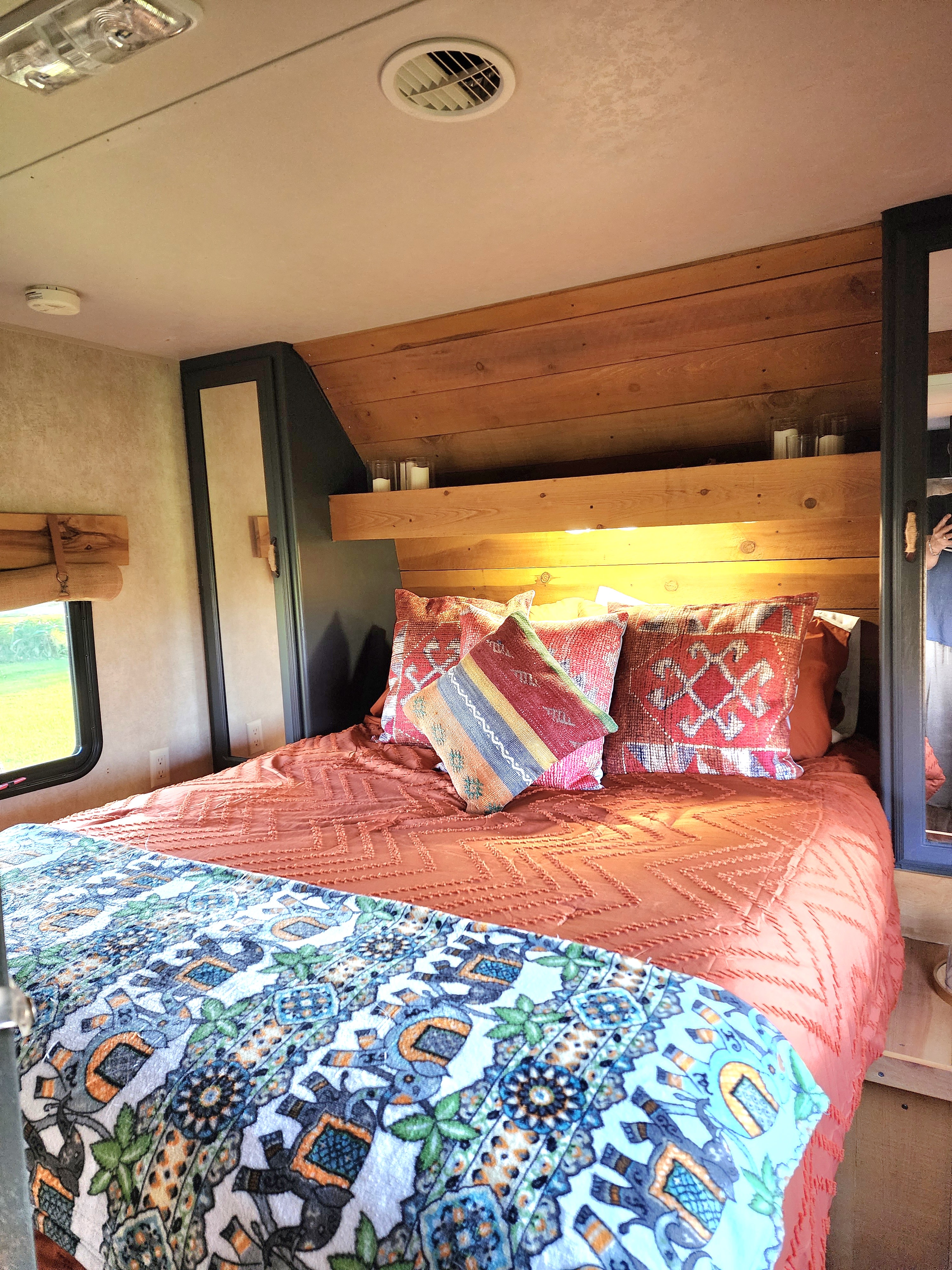 Step into this cozy RV rental bedroom, boasting a wooden headboard, vibrant pillows, and patterned bedding.. Forest River Wildwood 2017