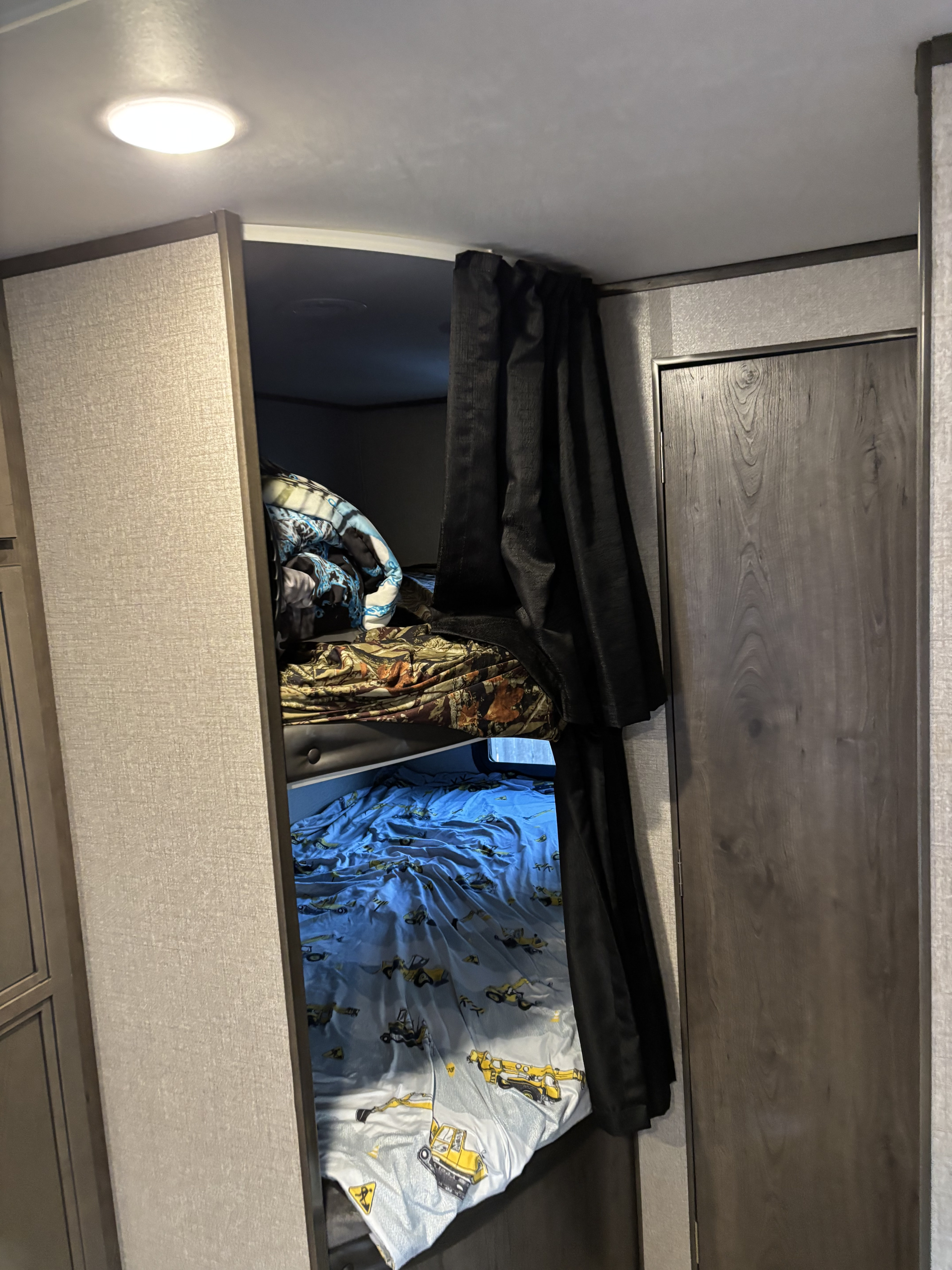 Cozy RV rental interior with bunk beds, including a lower bunk featuring construction vehicle sheets and a privacy curtain.. Jayco Jay Flight SLX Rocky Mountain Edition 2020