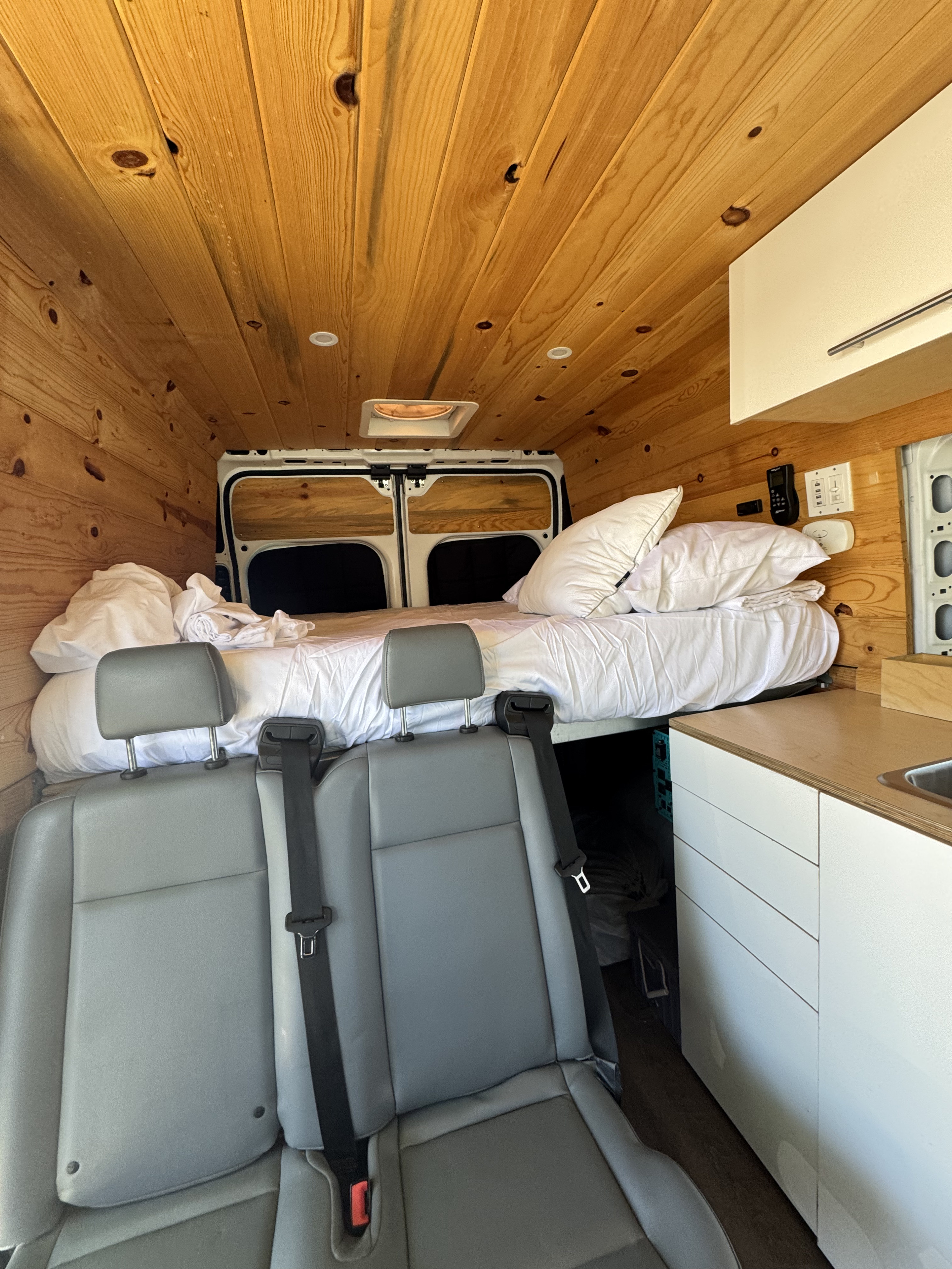 Interior of a cozy RV rental: wood-paneled walls, bed, kitchenette, and passenger seats.. Dodge B Van 2019