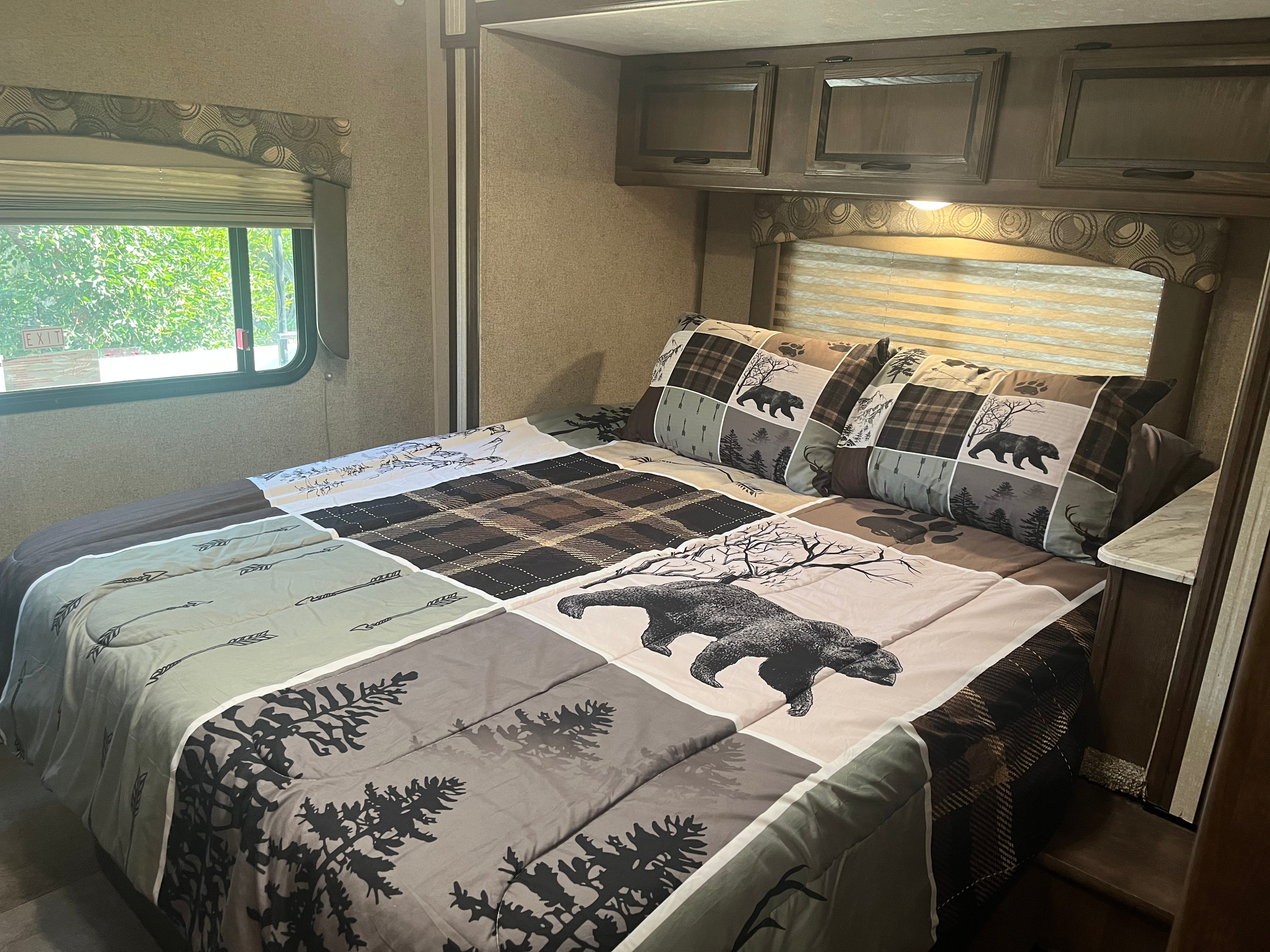 Cozy RV rental bedroom featuring bear & forest themed bedding, window views, and overhead cabinets for storage.. Coach House Freelander 2017