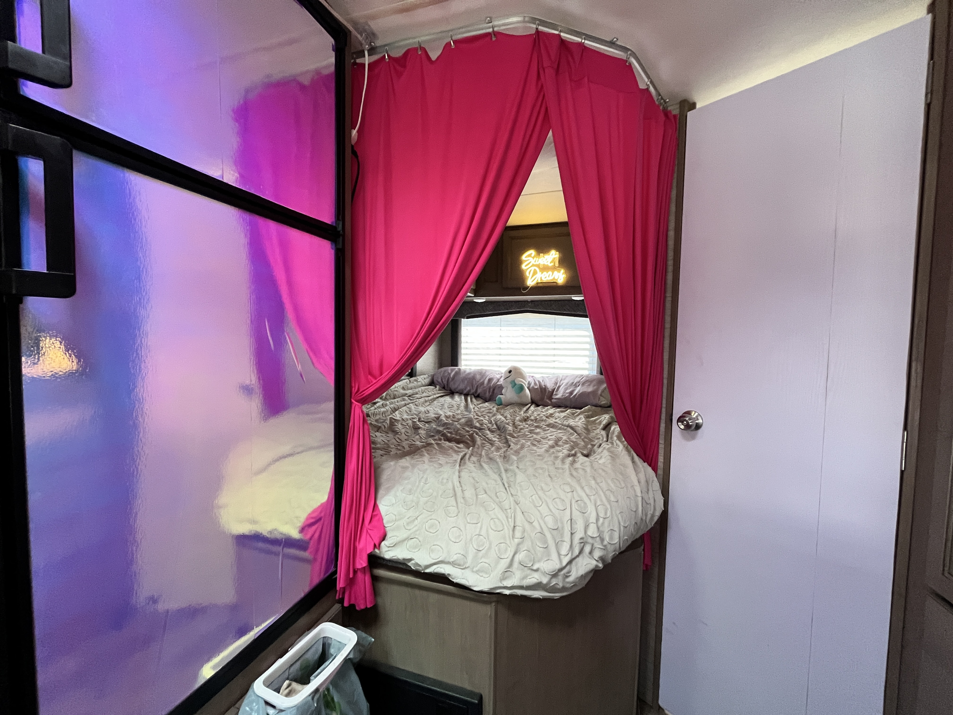 RV rental interior featuring a bed framed by vibrant pink privacy curtains, a "Sweet Dreams" neon sign, and a reflective panel.. Thor Chateau 2022
