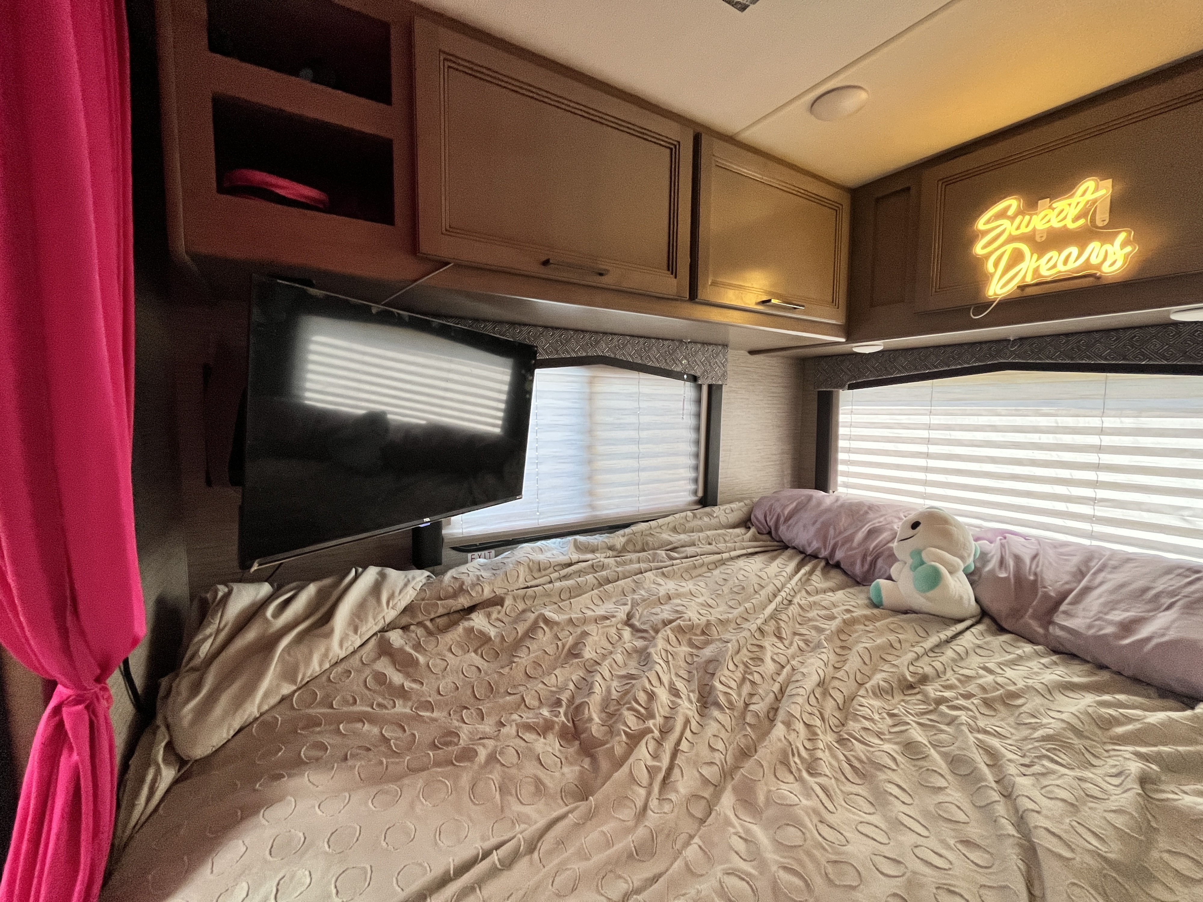 Cozy RV rental bedroom with beige bed, bright pink curtains, mounted TV, and a glowing "Sweet Dreams" sign.. Thor Chateau 2022