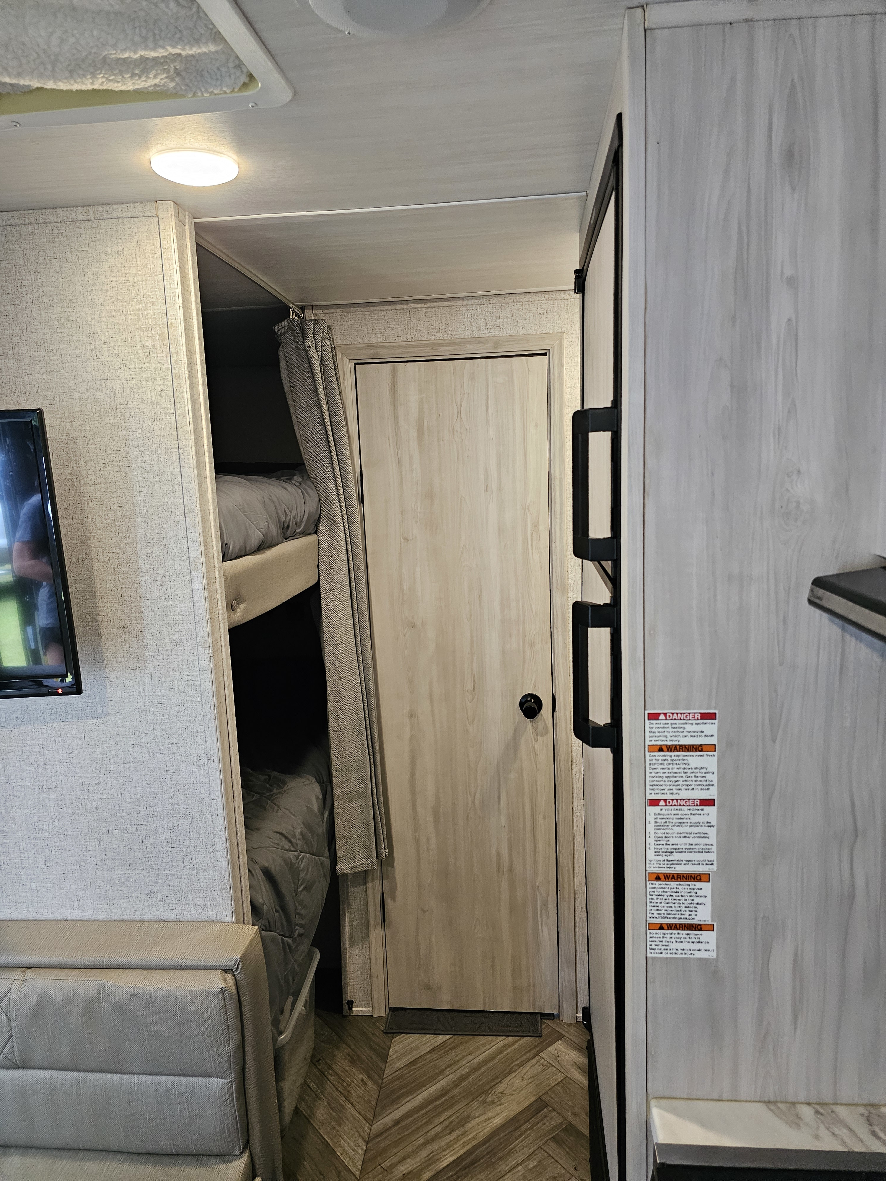 Compact RV rental interior showing bunk beds, a refrigerator, a TV, and sofa seating.. East to West Della Terra 2022