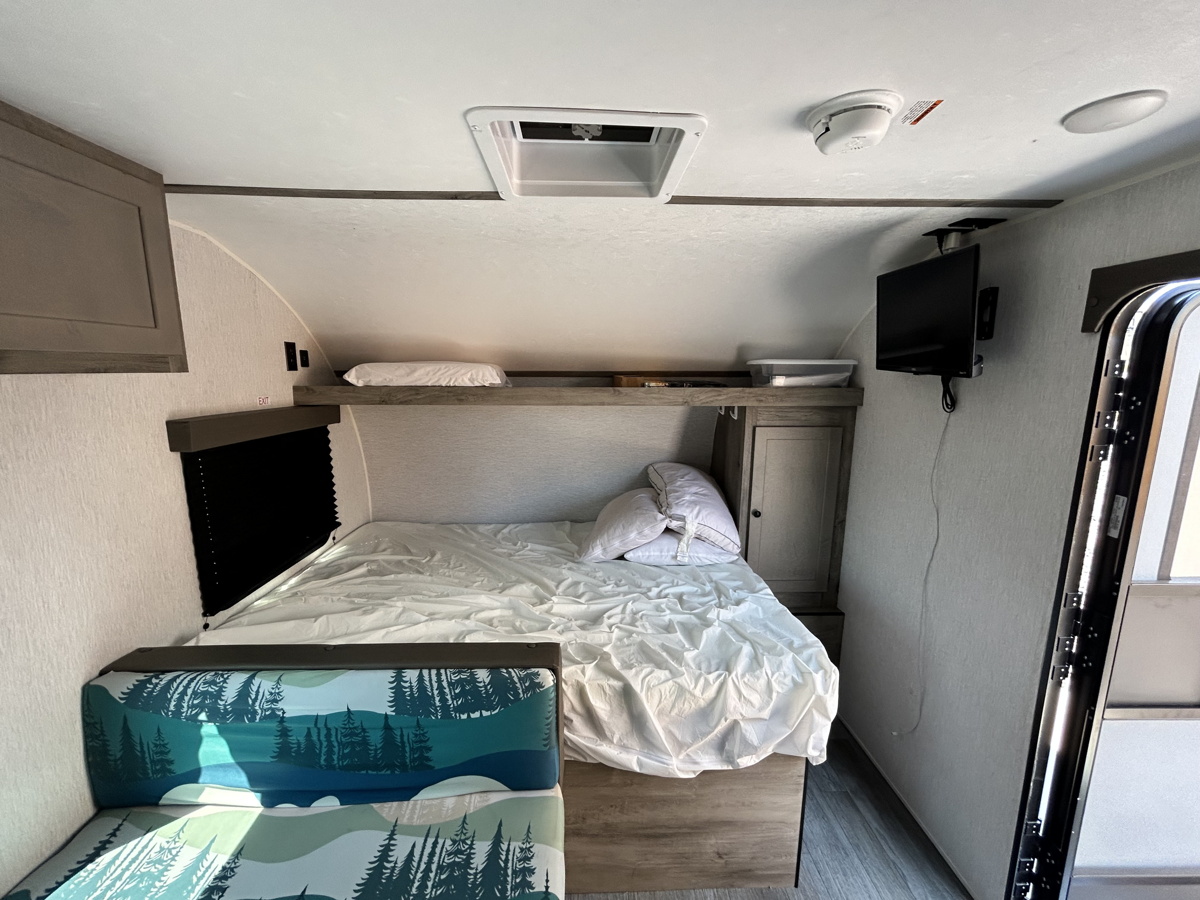 Explore this rv rental's interior: a comfortable bed, forest-patterned bench, TV, and convenient overhead storage.. Sunset Park & Rv Inc. 21bt 2026