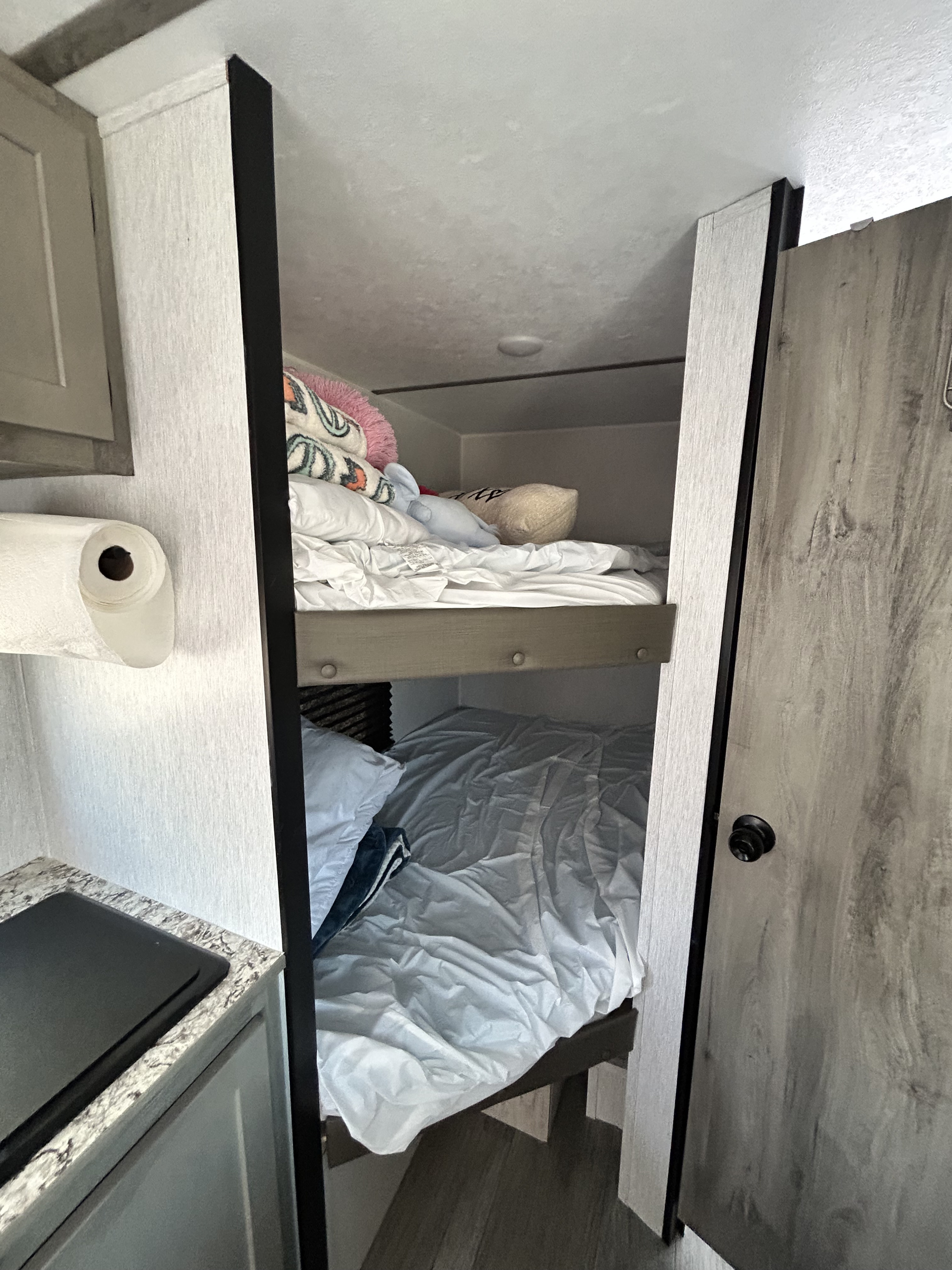 Cozy RV rental interior displays stacked bunk beds, a compact kitchen counter with stovetop, and a paper towel roll.. Sunset Park & Rv Inc. 21bt 2026