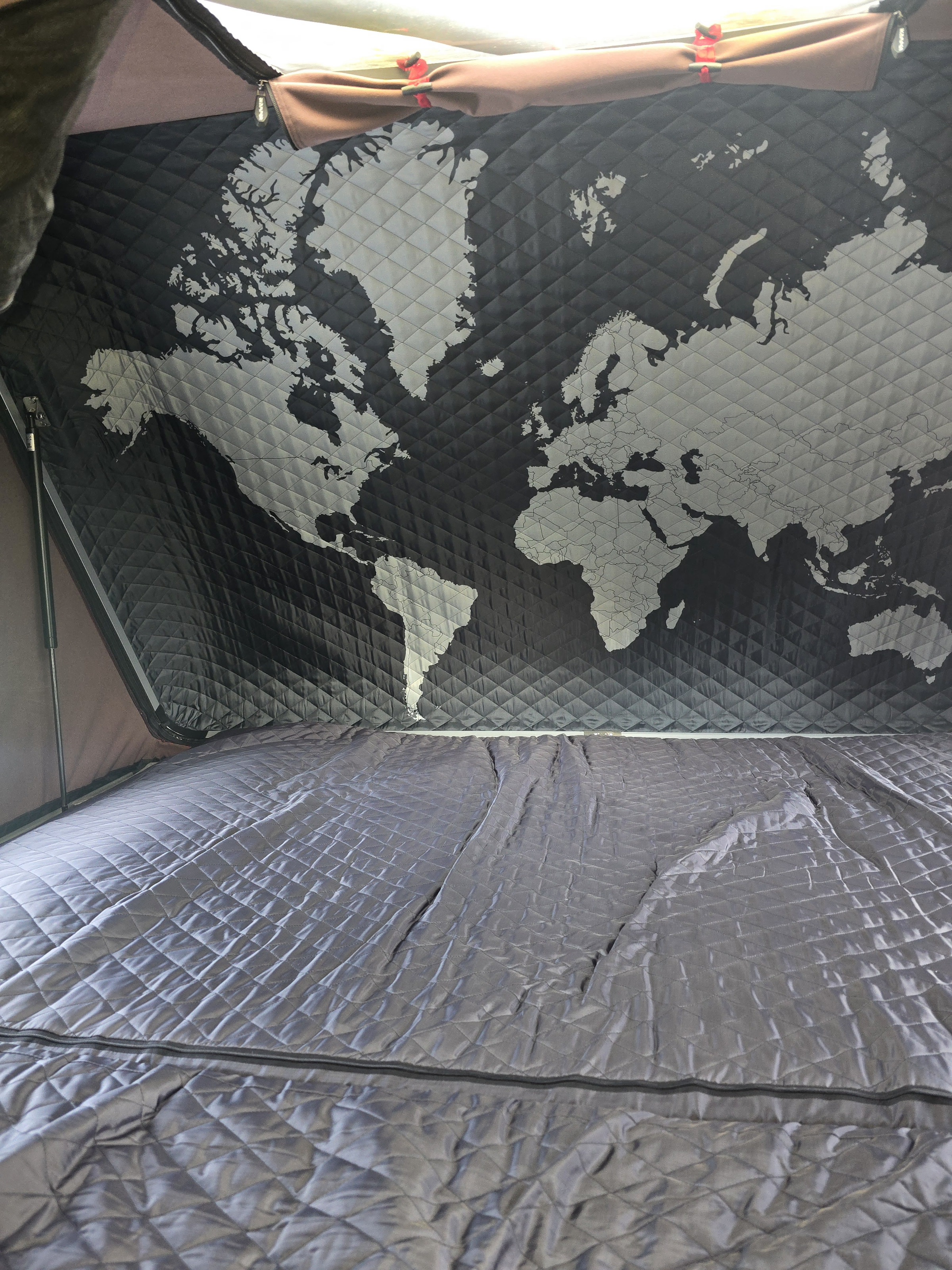 Cozy RV rental interior: a quilted world map adorns the ceiling above a matching, comfortable bed.. InTech RV Luna 2023