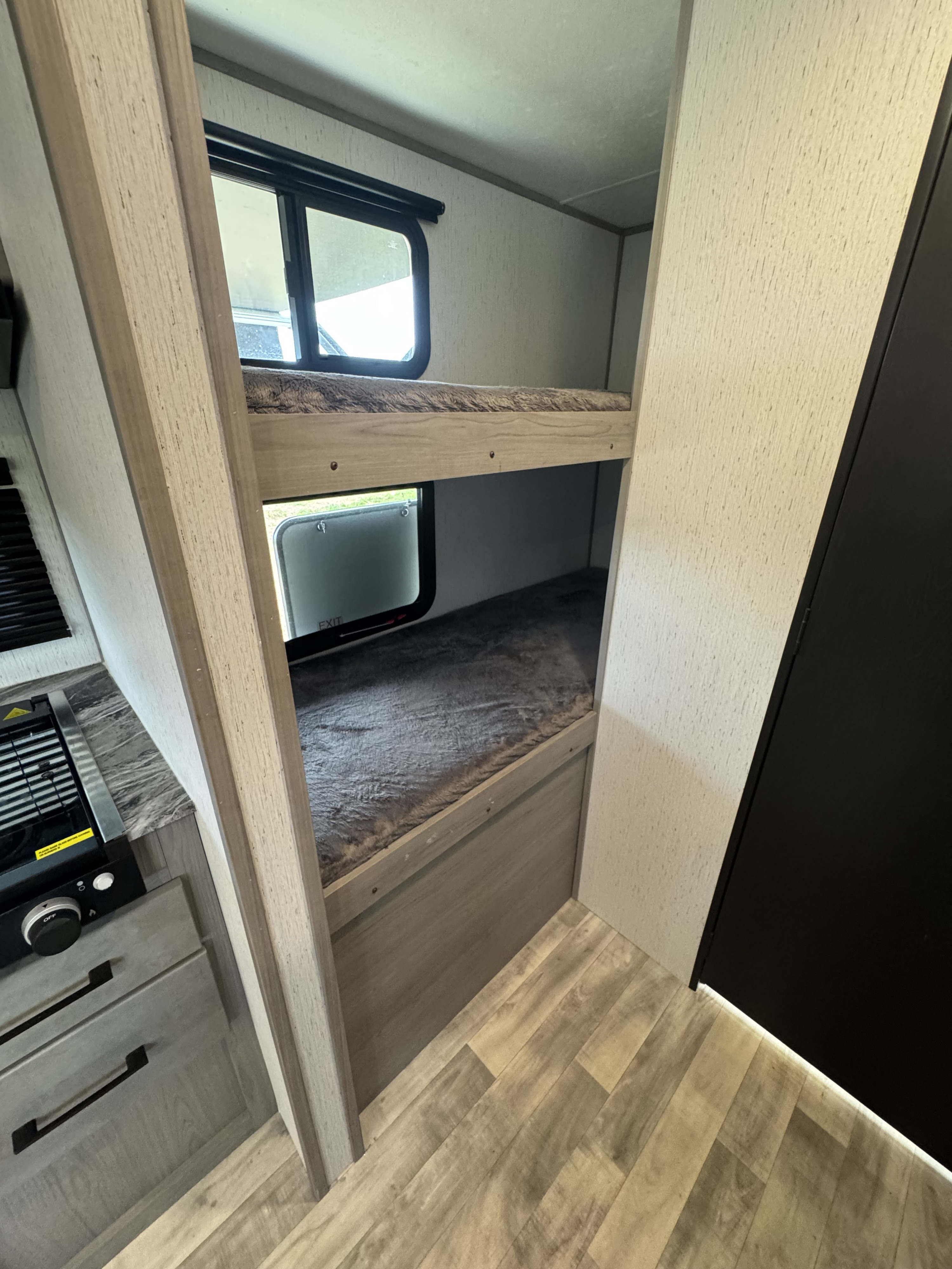 Inside an RV rental, featuring cozy bunk beds, a kitchen counter with a stove, and light wood flooring.. Dutchmen Kodiak Cub 2022