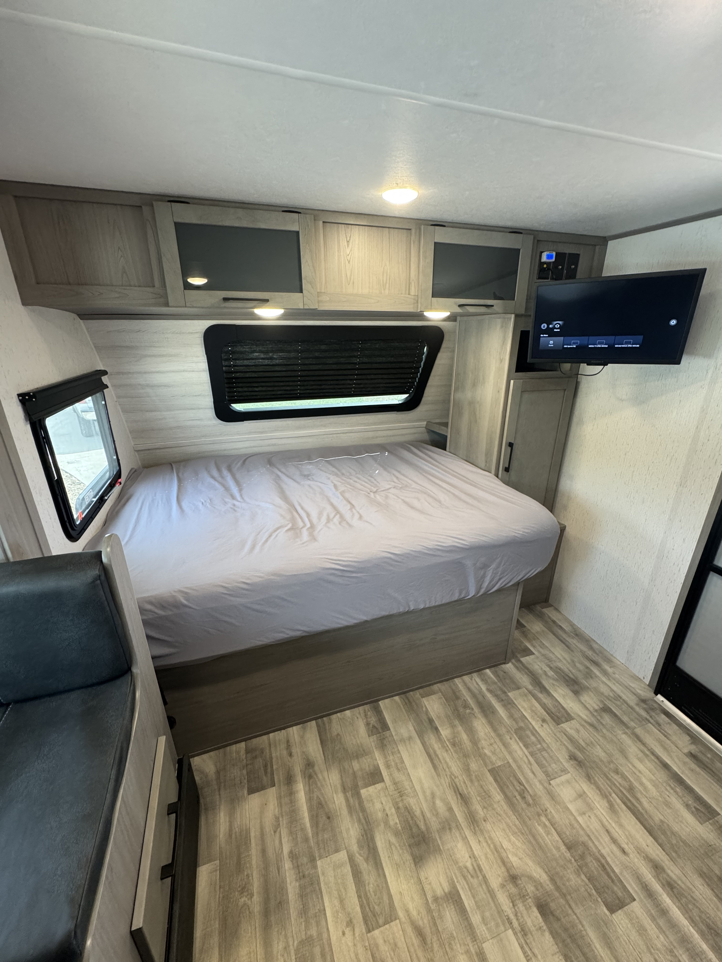 RV rental bedroom: light gray bed, wall-mounted TV, and wood-look cabinets, providing a comfortable mobile space.. Dutchmen Kodiak Cub 2022